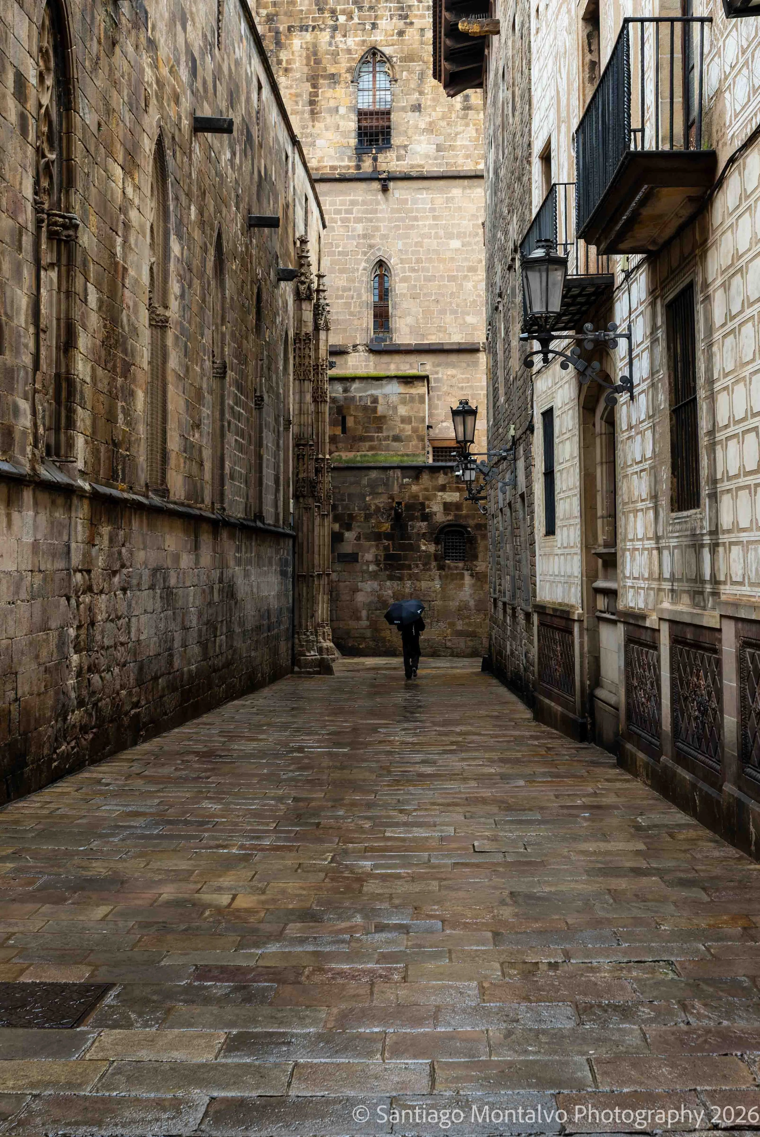A Figure in the Rain — Barcelona, Spain. A solitary moment along a rain-soaked stone passage.
