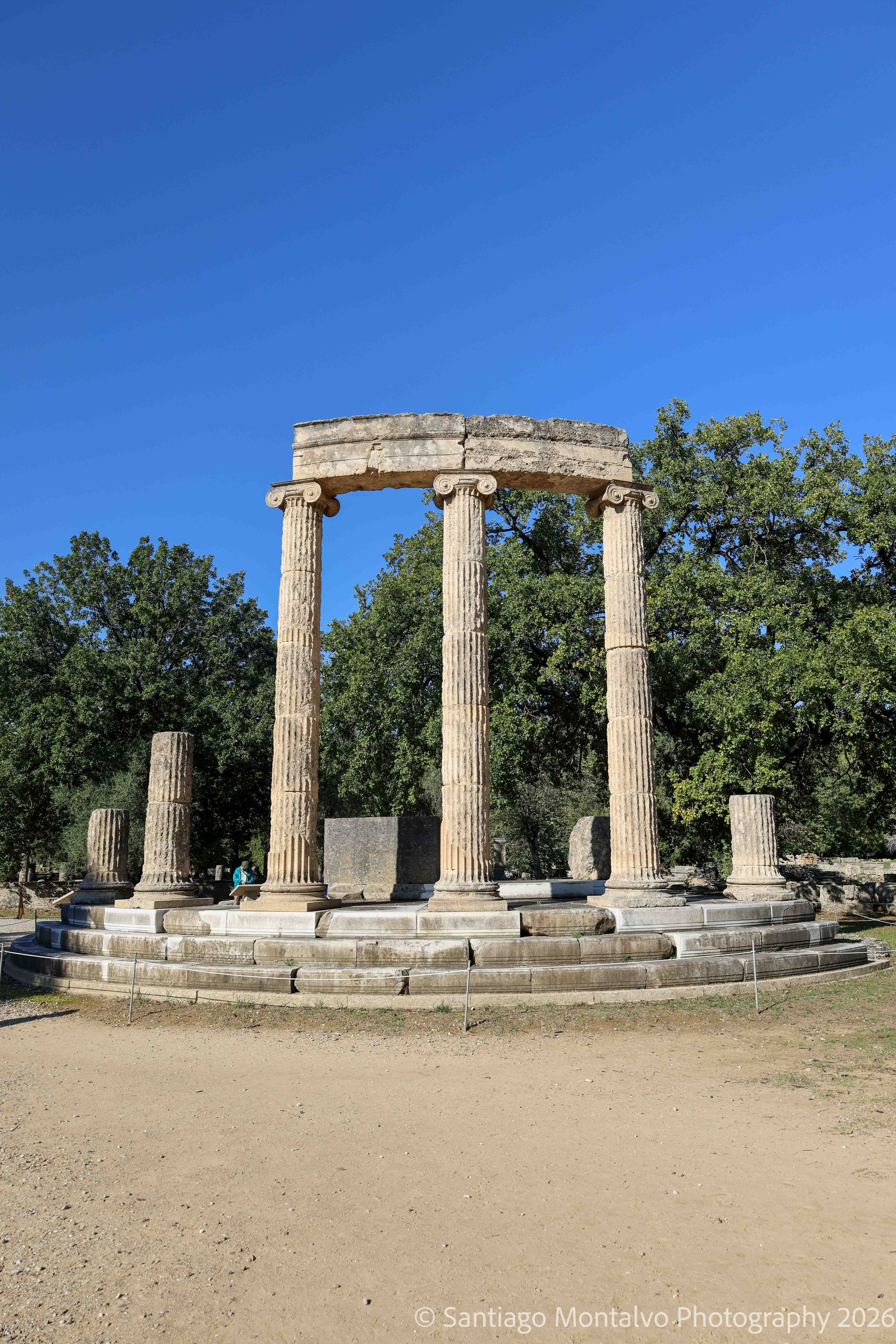 Columns of Antiquity — Olympia, Greece. Ancient stone columns rise against the rich blue sky, a testament to Greece's architectural heritage.