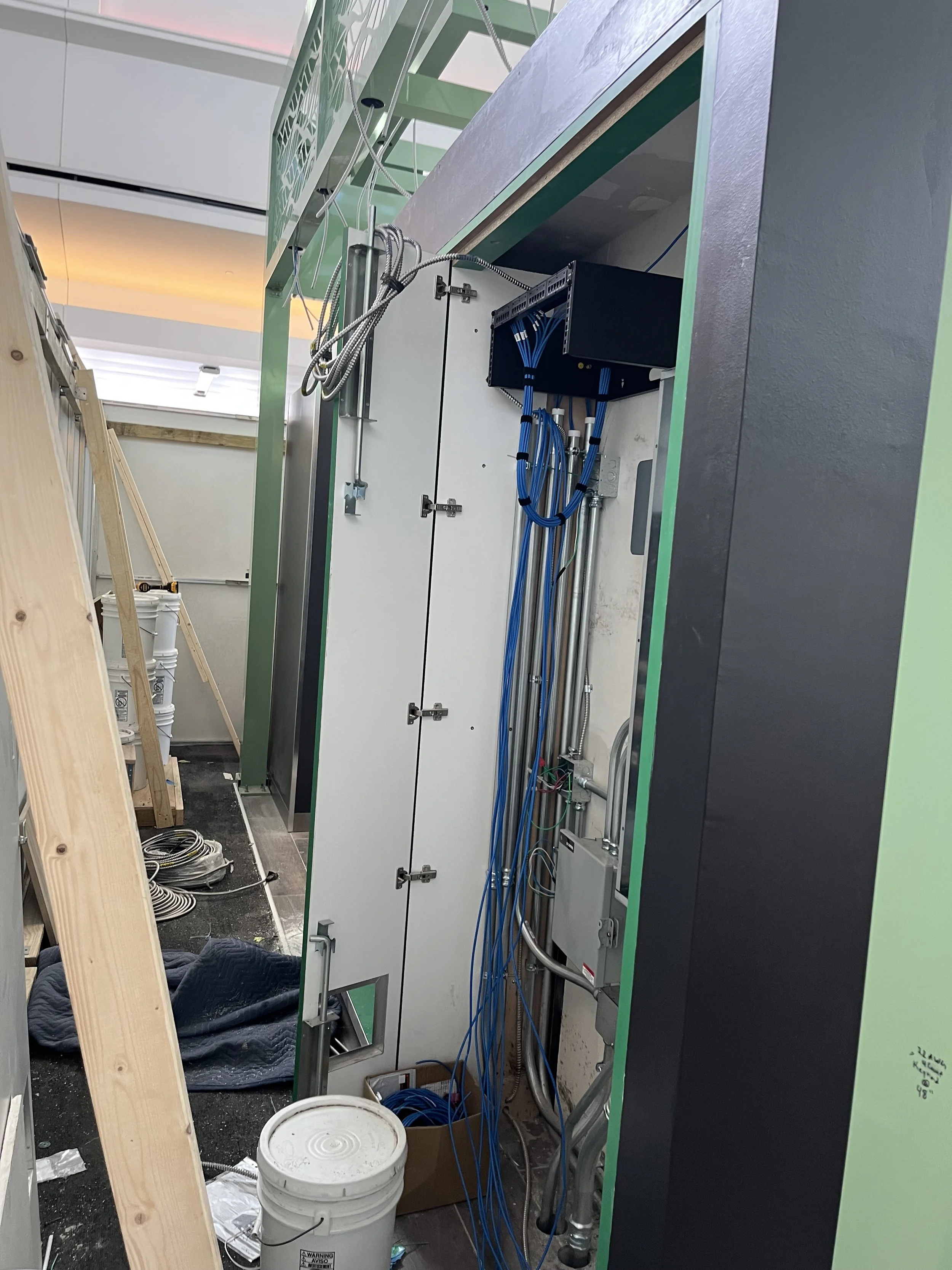 Construction site with electrical wiring and panels in progress, tools and materials scattered on the floor.