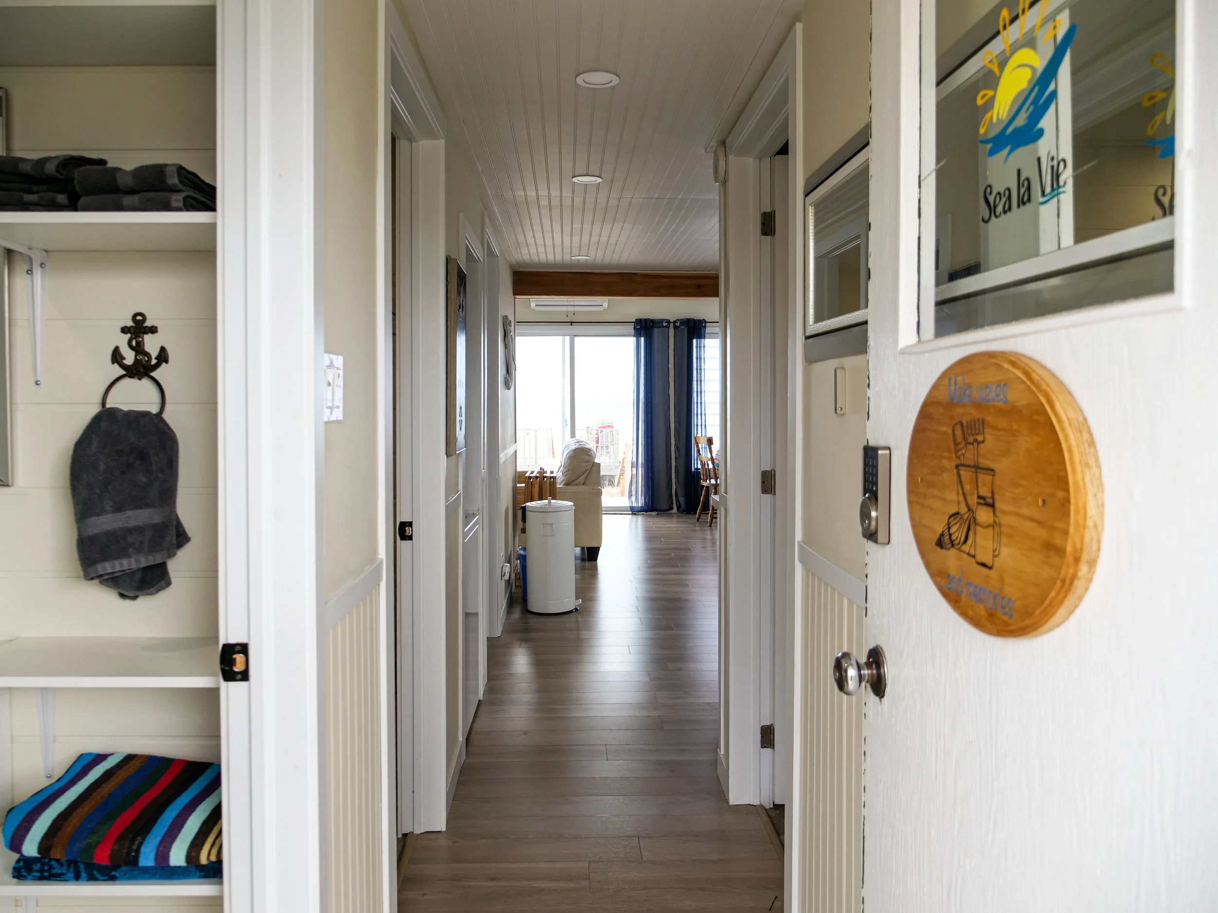 Interior view of a beach house hallway leading to a living room with sliding glass doors and balcony.
