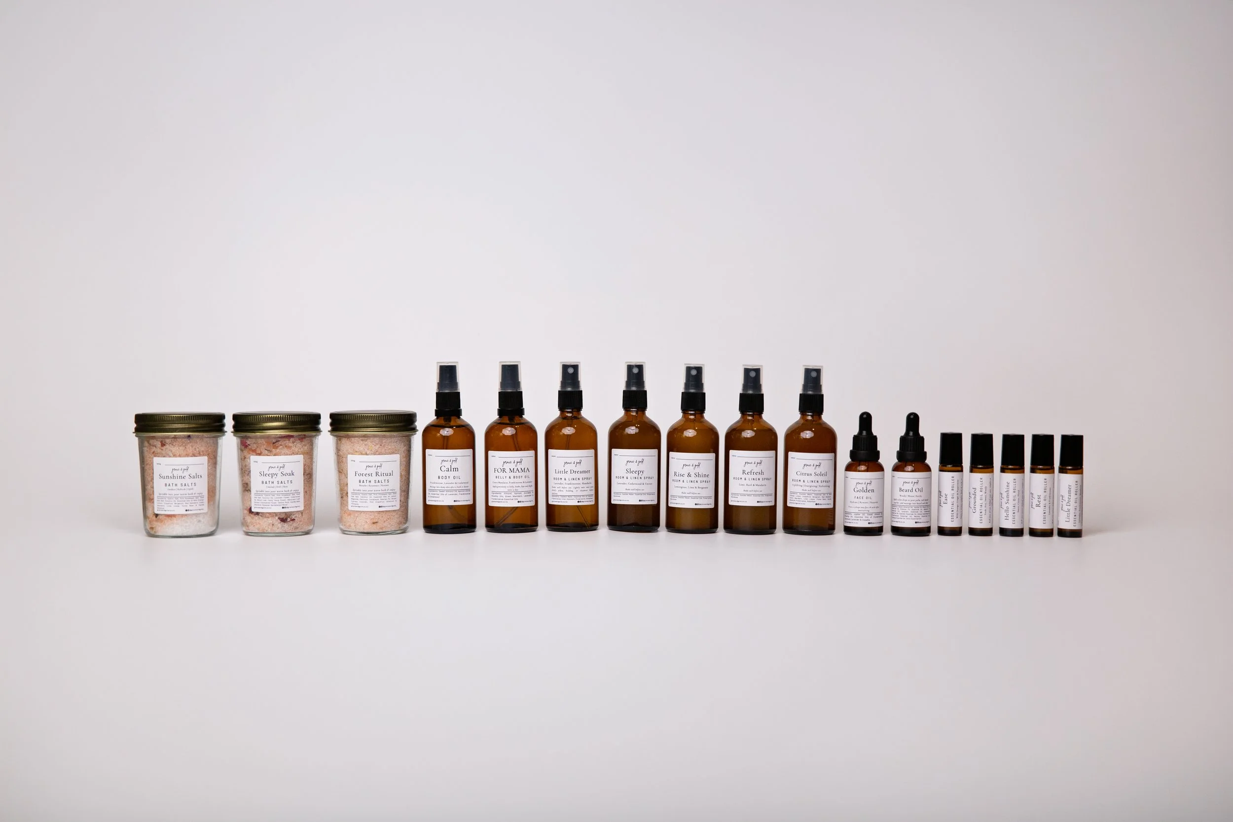 A row of bath salts jars and essential oil bottles arranged on a white background.
