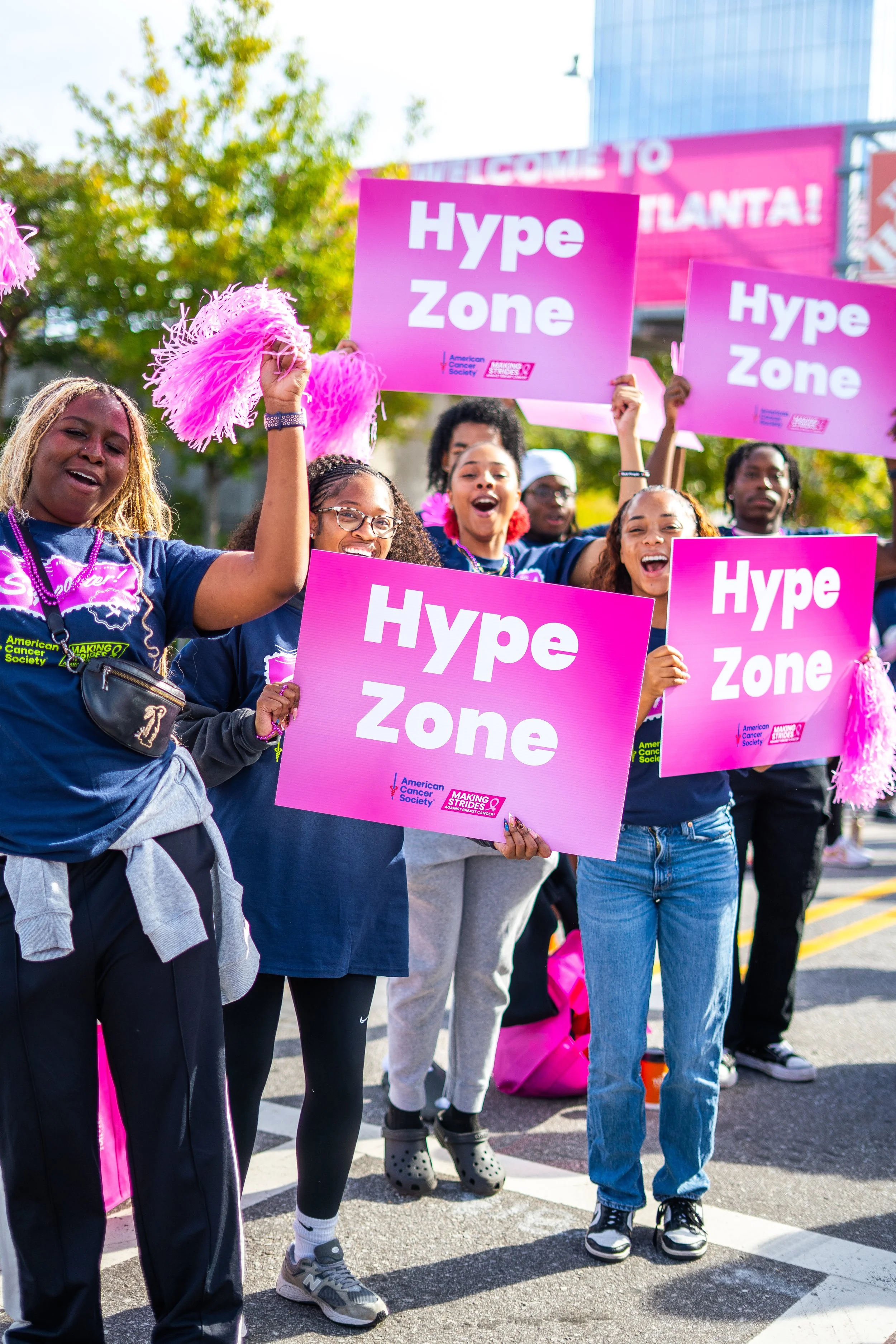 Group of people holding pink signs that say 'Hype Zone' during a march or rally, with smiles and cheering