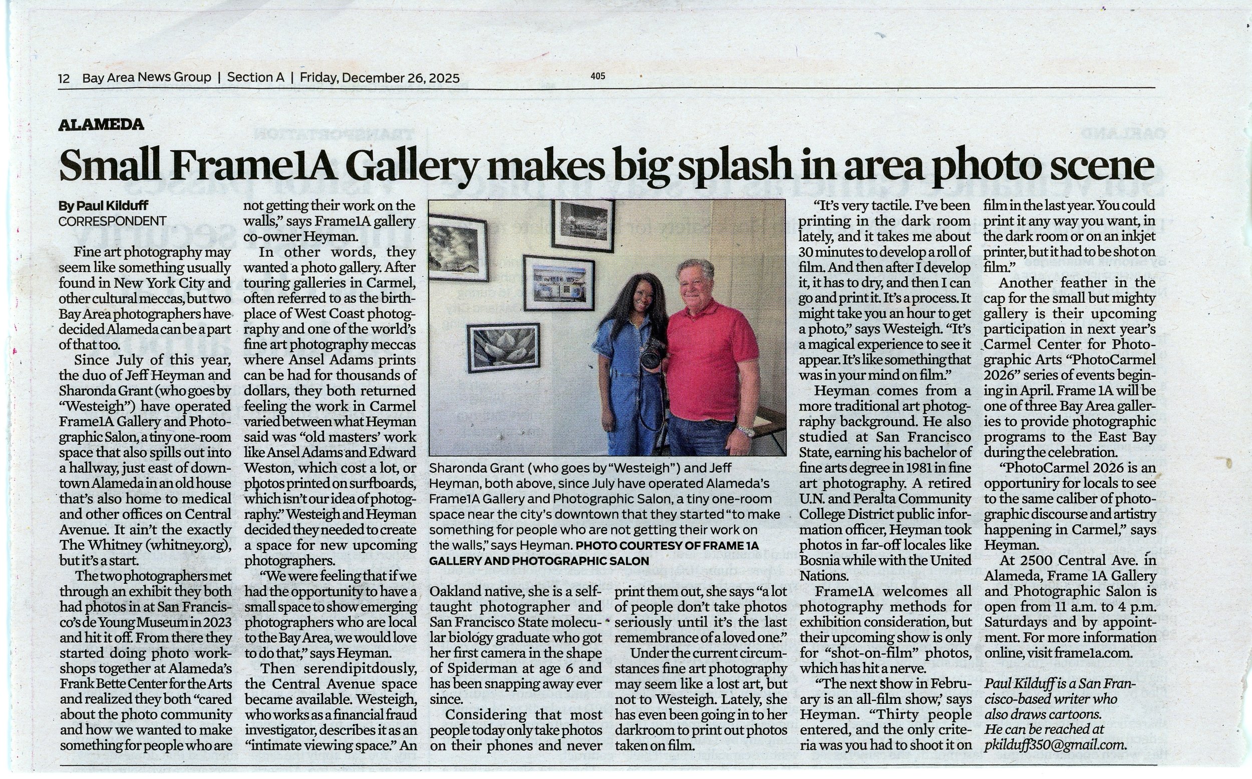 Photograph of a woman and a man standing inside an art gallery, in front of framed photographs on the wall. The woman is holding a camera, and both are smiling.