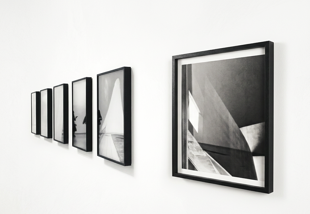 A series of black-framed photographs in black and white hanging on a white gallery wall.