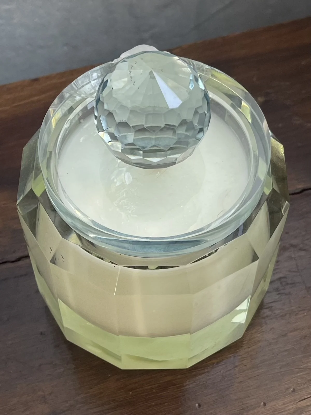 A decorative glass container with a faceted, diamond-like top, sitting on a wooden surface.