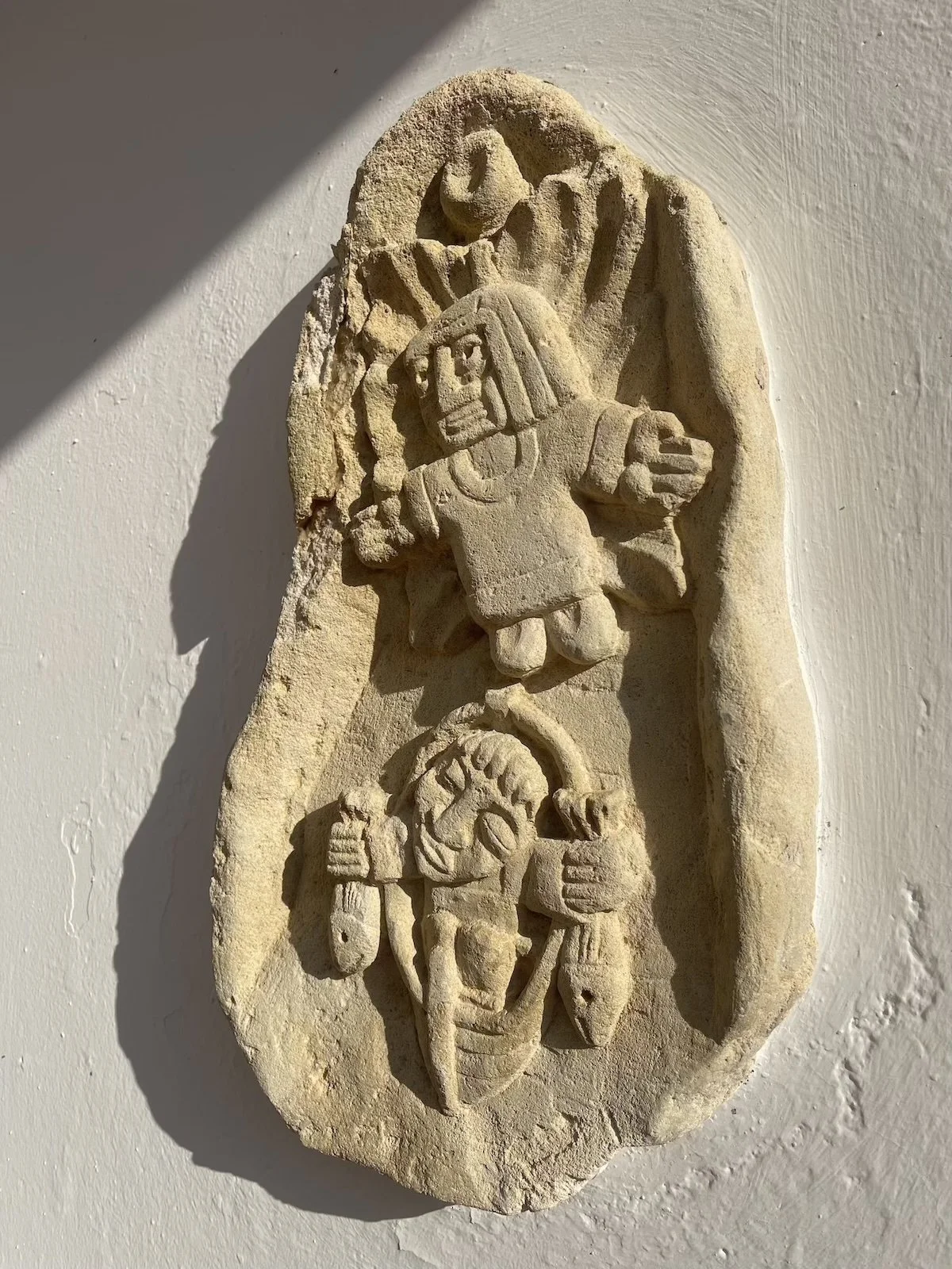 A carved stone relief depicting two figures; one figure appears to be an Egyptian pharaoh or deity, with a headdress, holding a scepter, and the other figure is smaller, possibly a servant or attendant, holding a staff or spear.