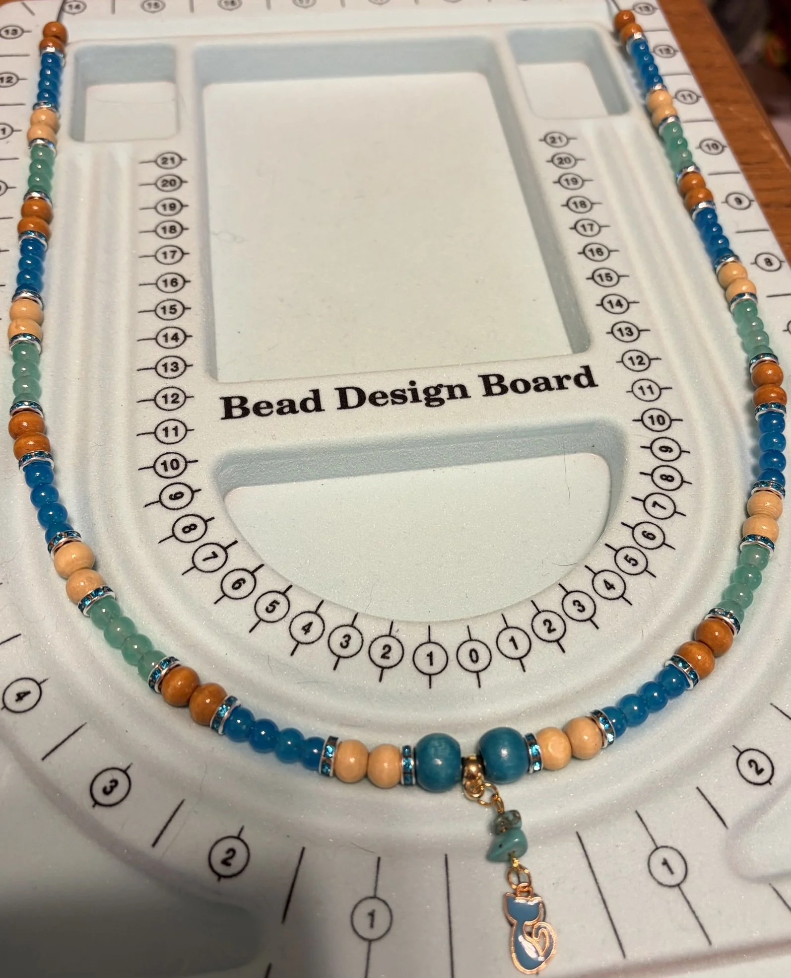 Colorful beaded necklace with beads in shades of blue, teal, beige, and gold, displayed on a bead design board.