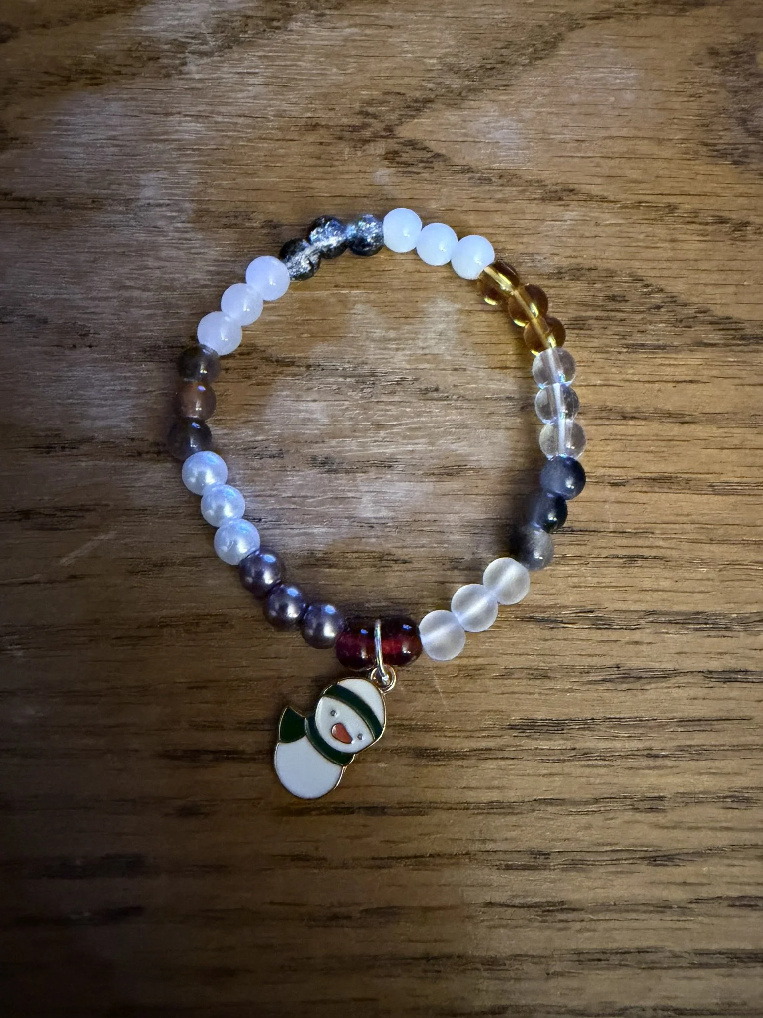 A beaded bracelet with various colored beads and a snowman charm on a wooden surface.