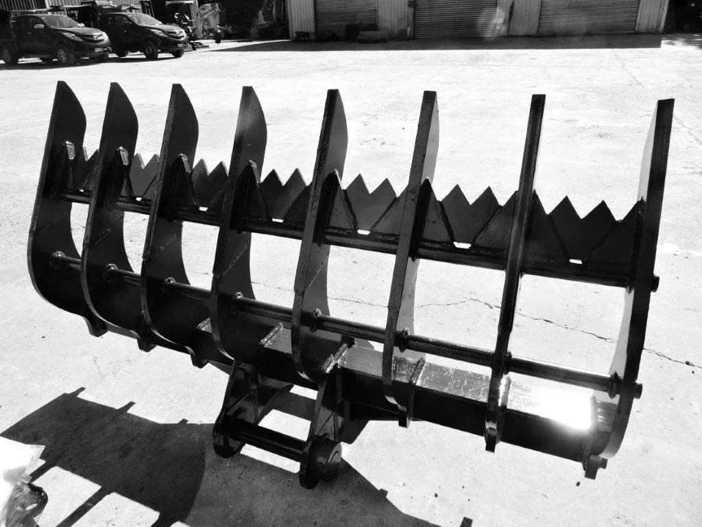 A large black agricultural tillage tool or implement with multiple sharp teeth and curved blades, resting on a concrete surface in an open lot with parked cars and warehouse buildings in the background.
