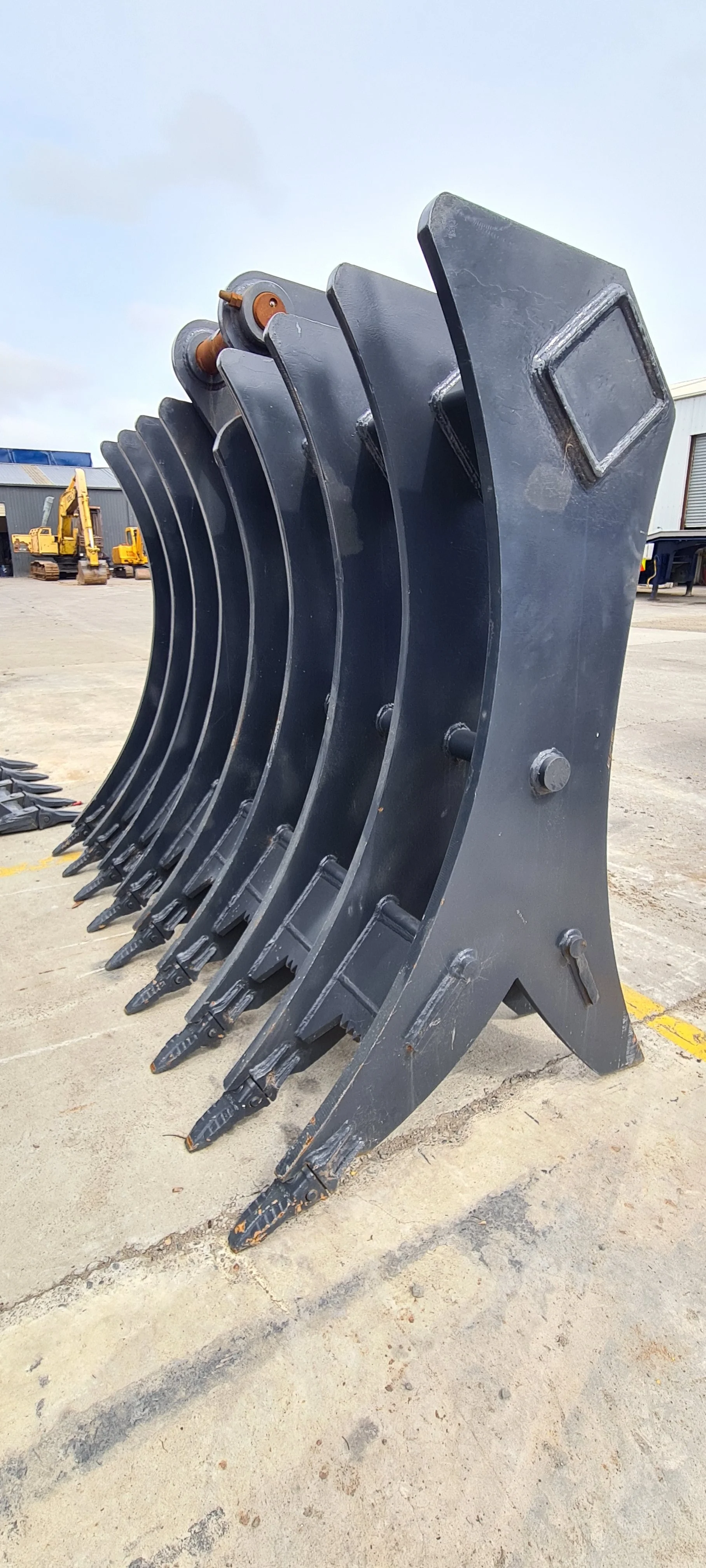 Large excavator buckets parked in a row at an industrial site with construction equipment in the background.
