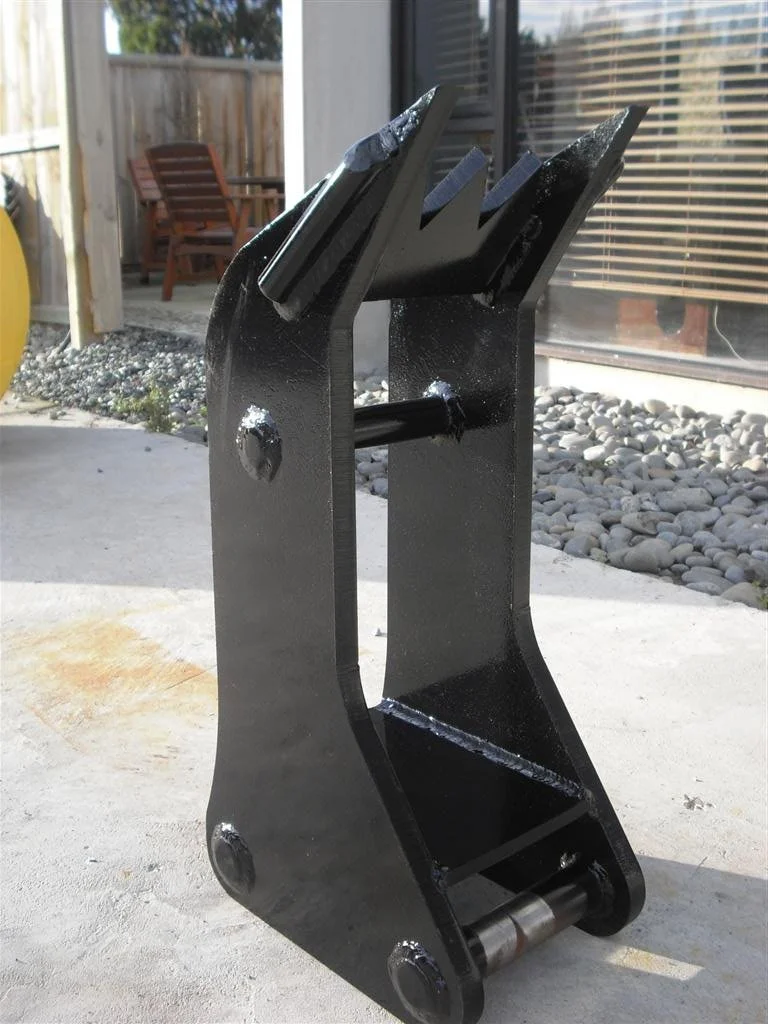 A large, black, metal excavator bucket attachment placed on a concrete patio outdoors.