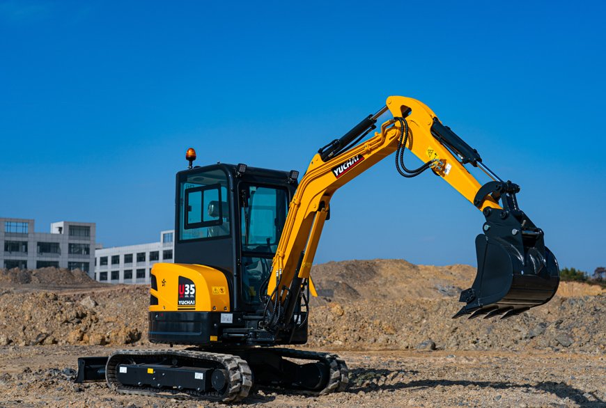A yellow and black Yuchai mini excavator working on a dirt construction site with buildings in the background and clear blue skies.