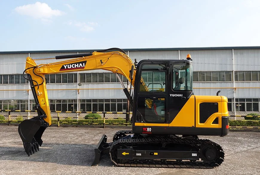 Yellow Yuchai YC80 mini excavator with a black bucket attachment parked outdoors near a building with large windows.