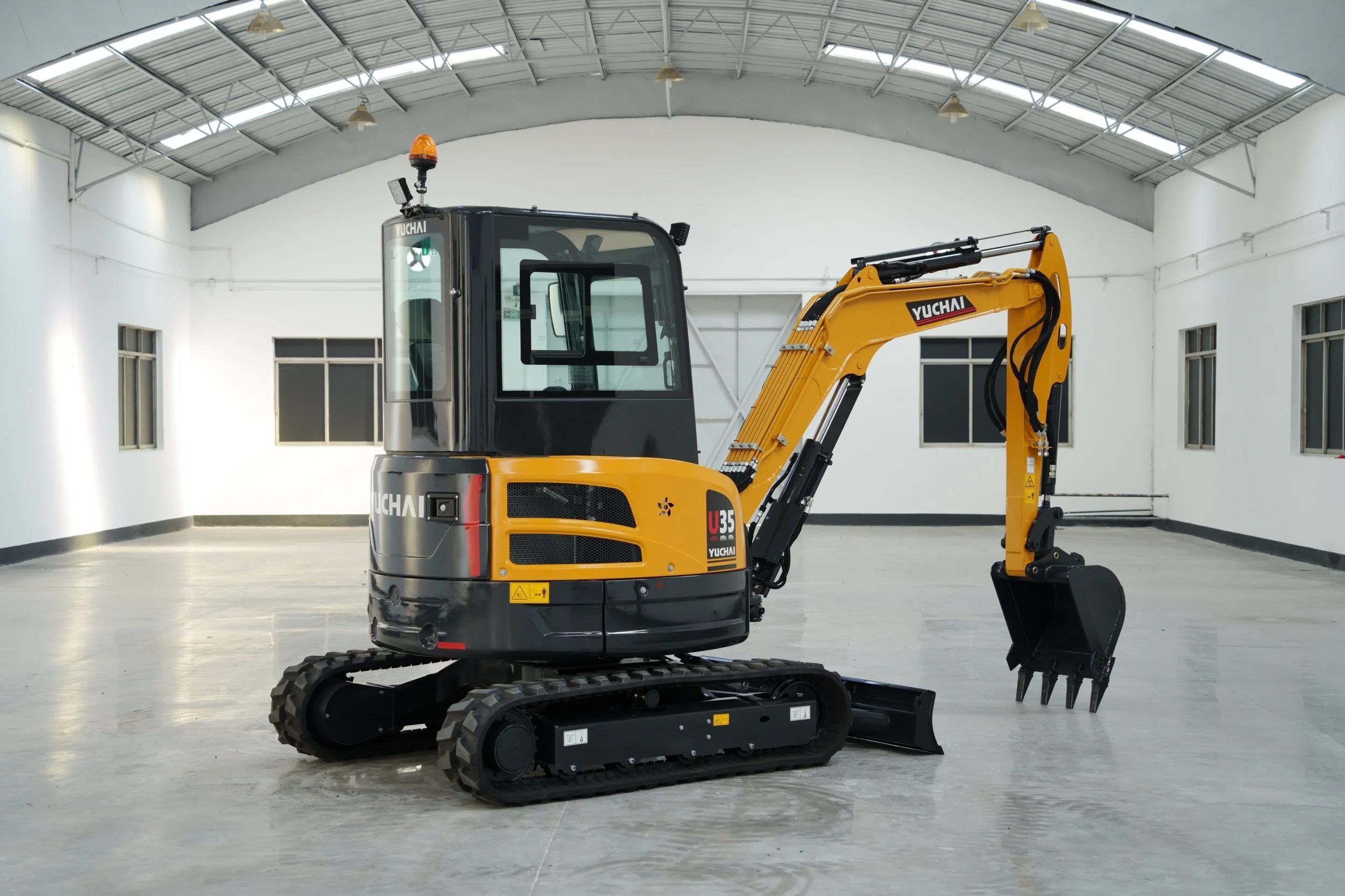 A small yellow and black Yuchi mini excavator inside a spacious, well-lit warehouse with high ceilings and large windows.