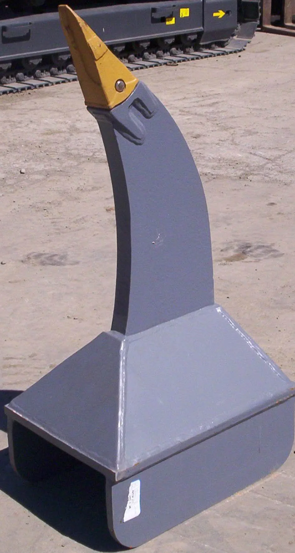 A modern metal sculpture resembling a whale with a yellow tail fin, standing on a square base, outdoors on sandy ground.
