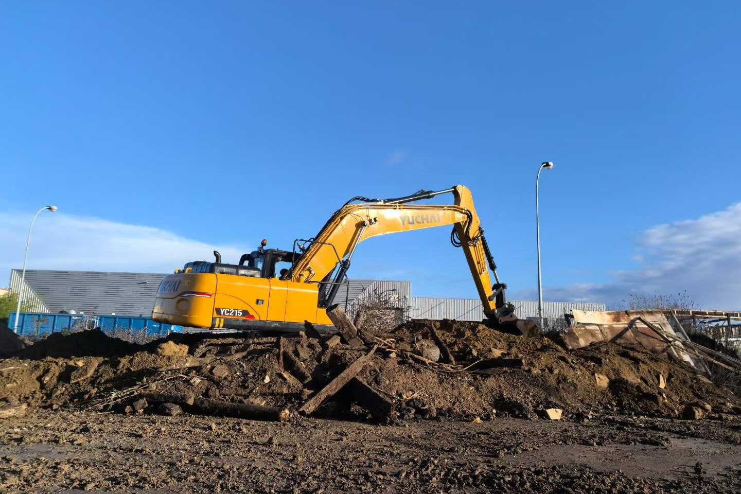A yellow excavator on a construction site moving dirt under a blue sky.