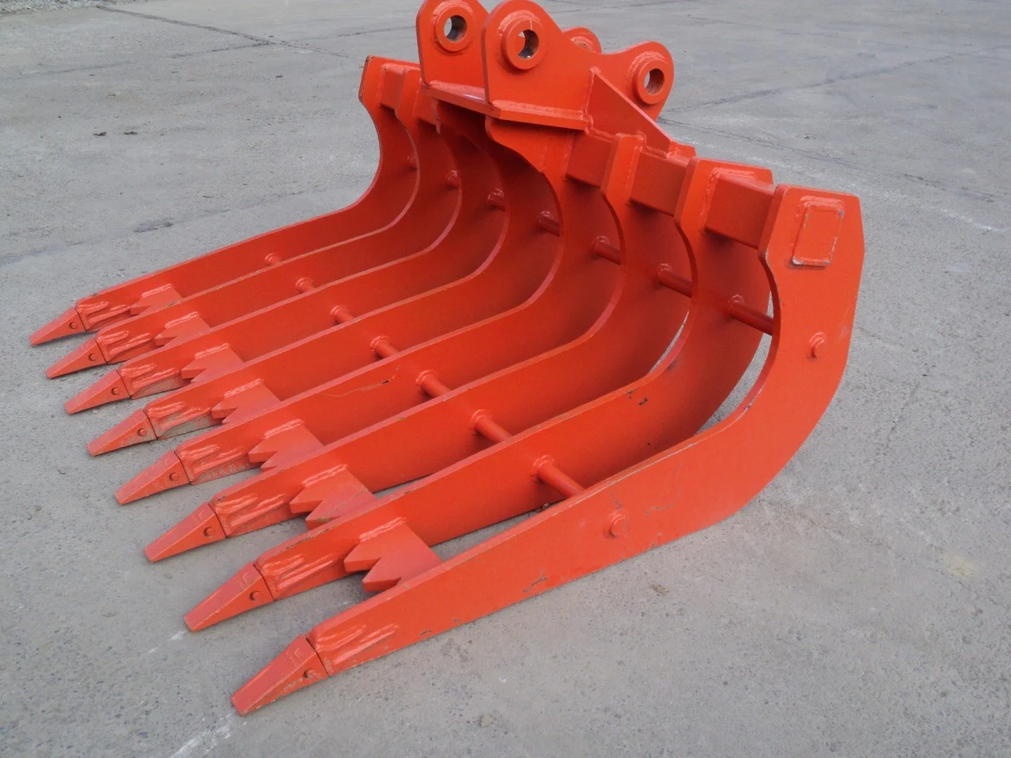 A large orange excavator bucket attachment placed on a concrete surface.