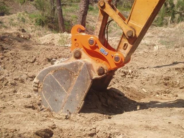 Close-up of a yellow and orange excavator bucket removing soil on a construction site.