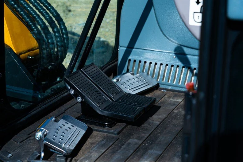 Close-up of the foot pedals inside the cabin of an excavator or heavy machinery, including accelerator and brake pedals.