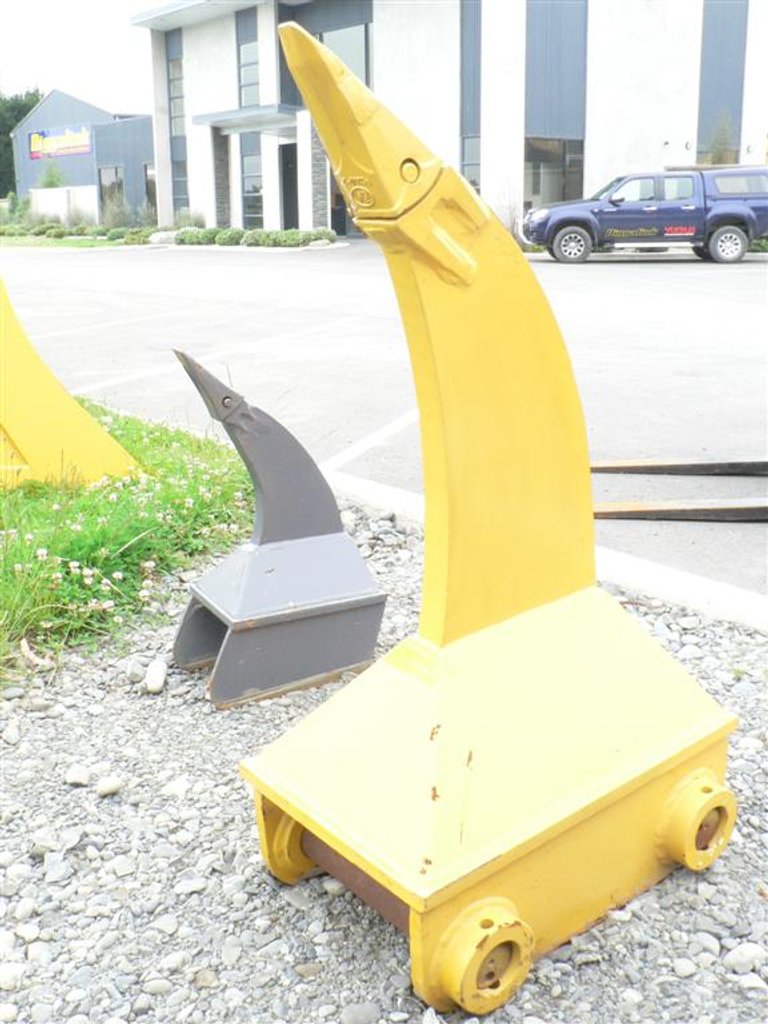 Yellow mechanical dolphin sculpture with a sail-shaped dorsal fin, located outdoors on gravel near a building and parking lot.