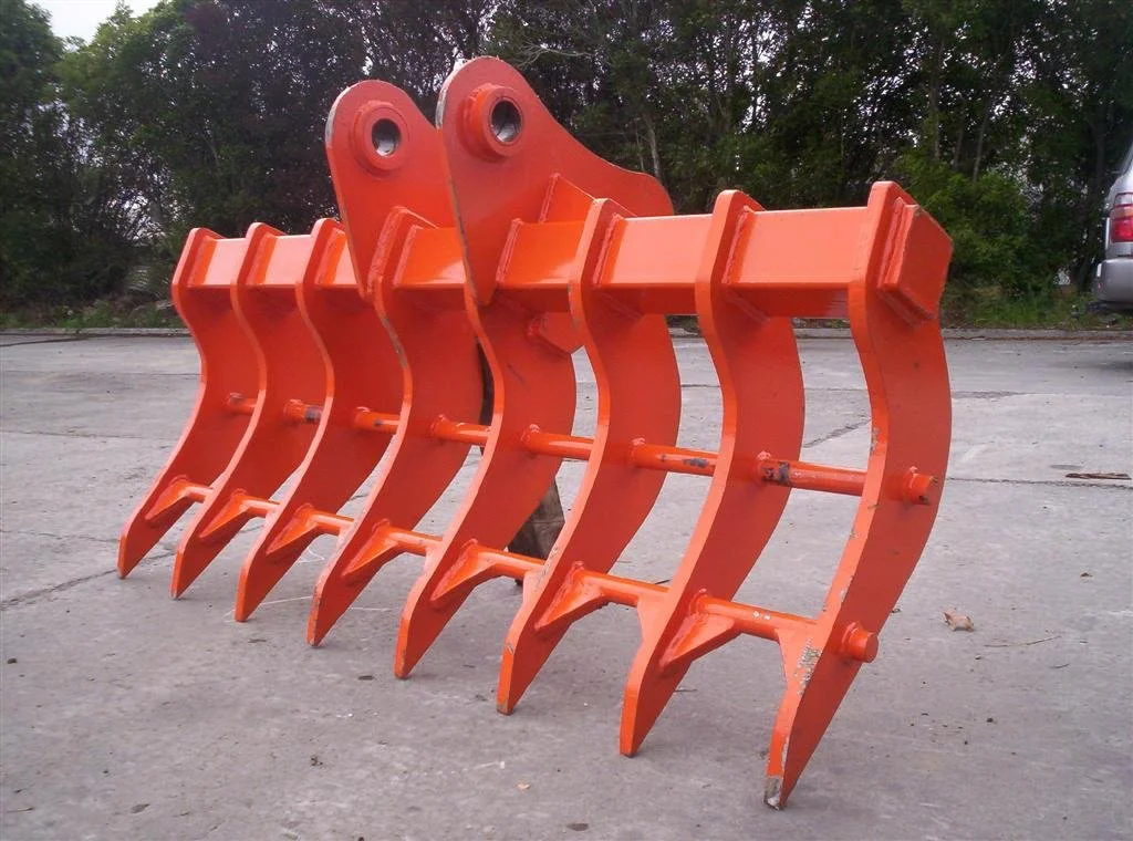 Orange excavator bucket attachment on concrete ground with trees and a parked vehicle in the background.