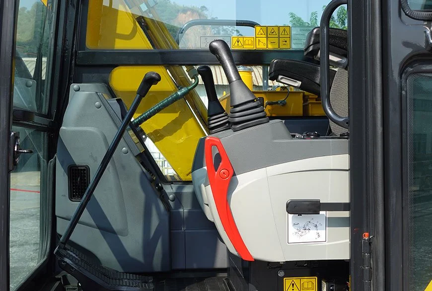 Close-up of the interior cabin of a construction excavator, showing the seat, control levers, and warning stickers.