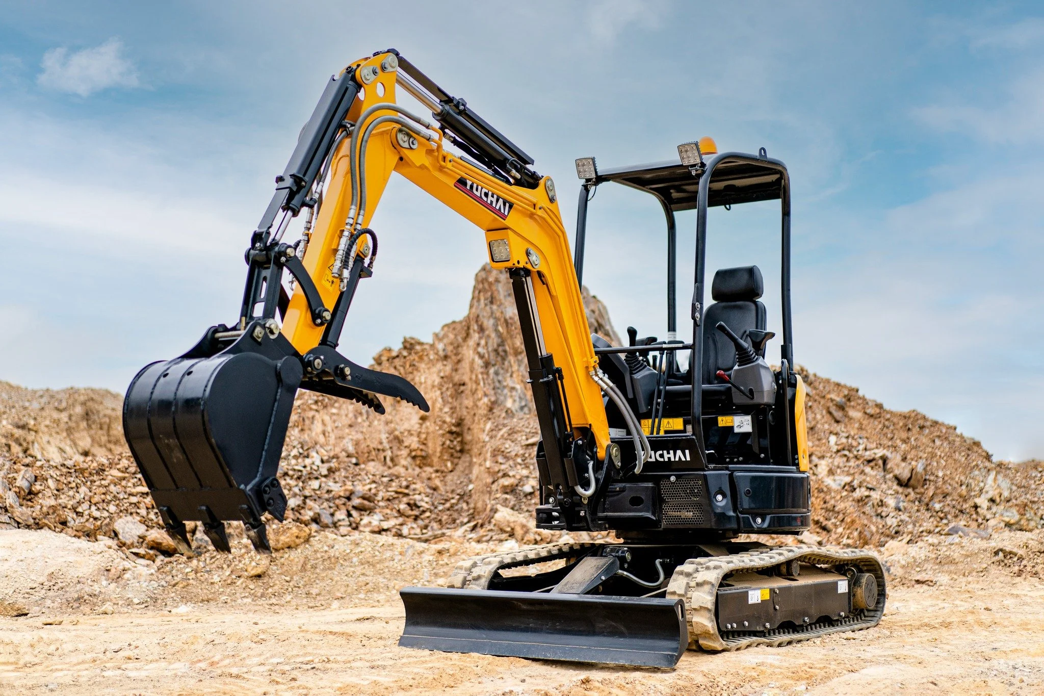 A yellow and black mini excavator at a construction site with dirt and rocks around, under a cloudy sky.