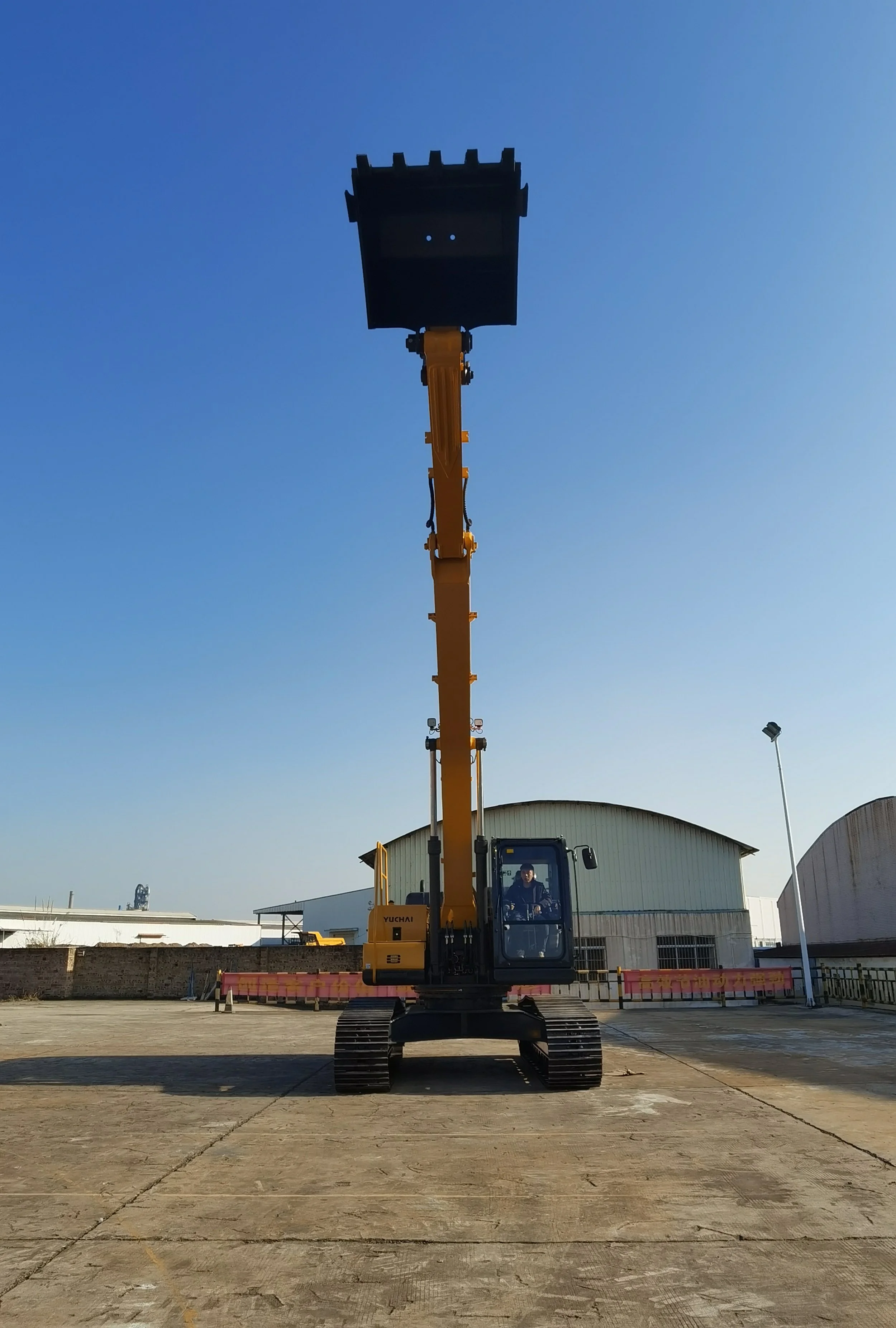 A yellow telescopic boom lift elevated on tracks in an outdoor industrial area under a clear blue sky, with warehouses and streetlights in the background.