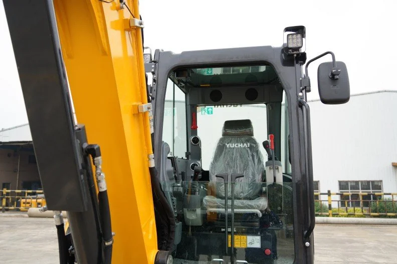 Front view of a Yuchai excavator, showing the operator's cabin with controls and seat inside, outdoors at a construction site or equipment yard.