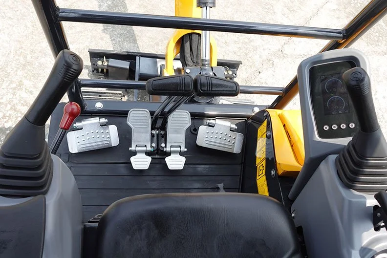 View from the operator's seat of construction equipment, showing two joysticks, pedals, and control panel, with a yellow safety bar in the background.