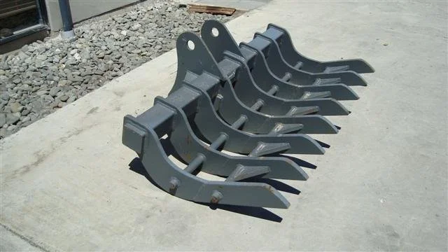 Five black excavator buckets lined up on a concrete surface outdoors.