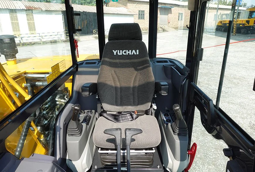 Interior of a construction vehicle with control levers, a Yuchai branded seat, and a view of construction equipment outside.