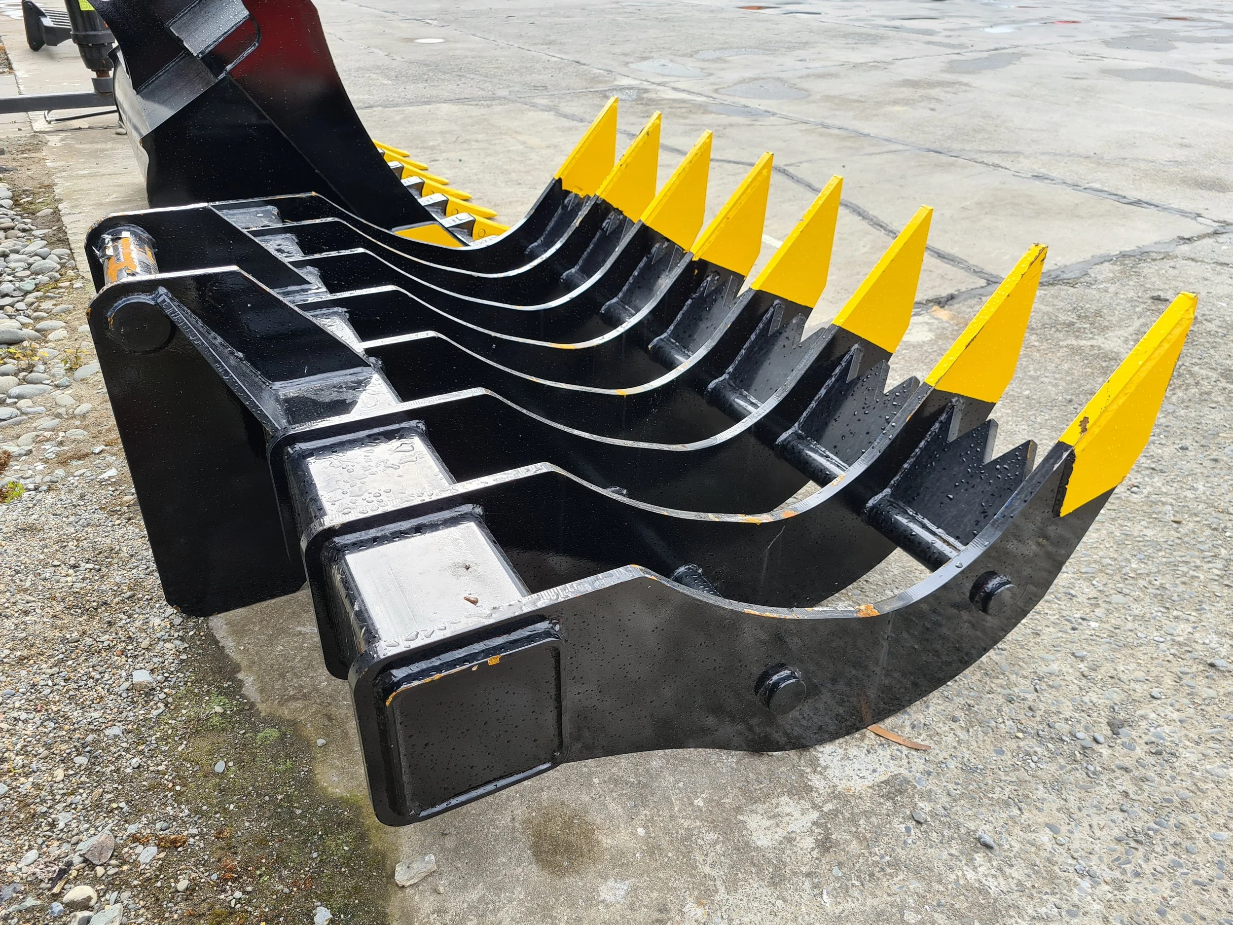 A black metal bucket with yellow metal guards on the edges, placed on a gravel and concrete surface.
