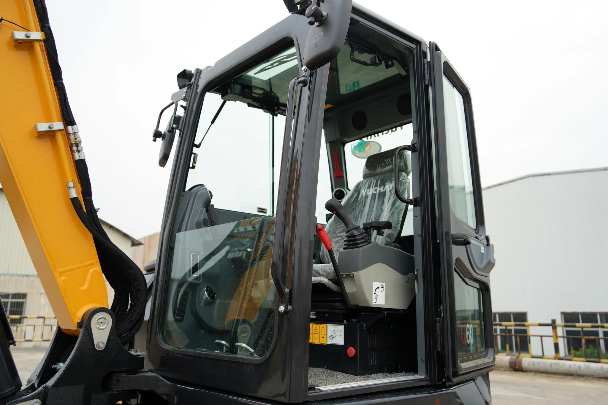 Close-up of a construction vehicle's cabin, showing the glass door, black frame, and a yellow arm with hydraulic hoses attached.