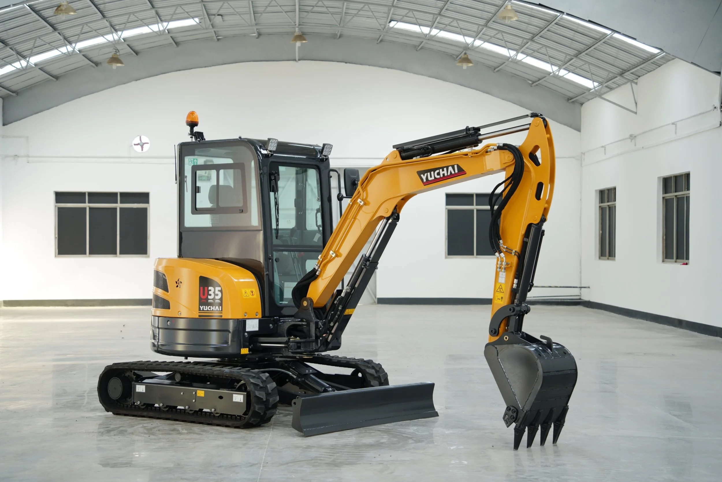 A yellow and black Yuchai mini excavator inside a large empty industrial building with a high metal roof and white walls.