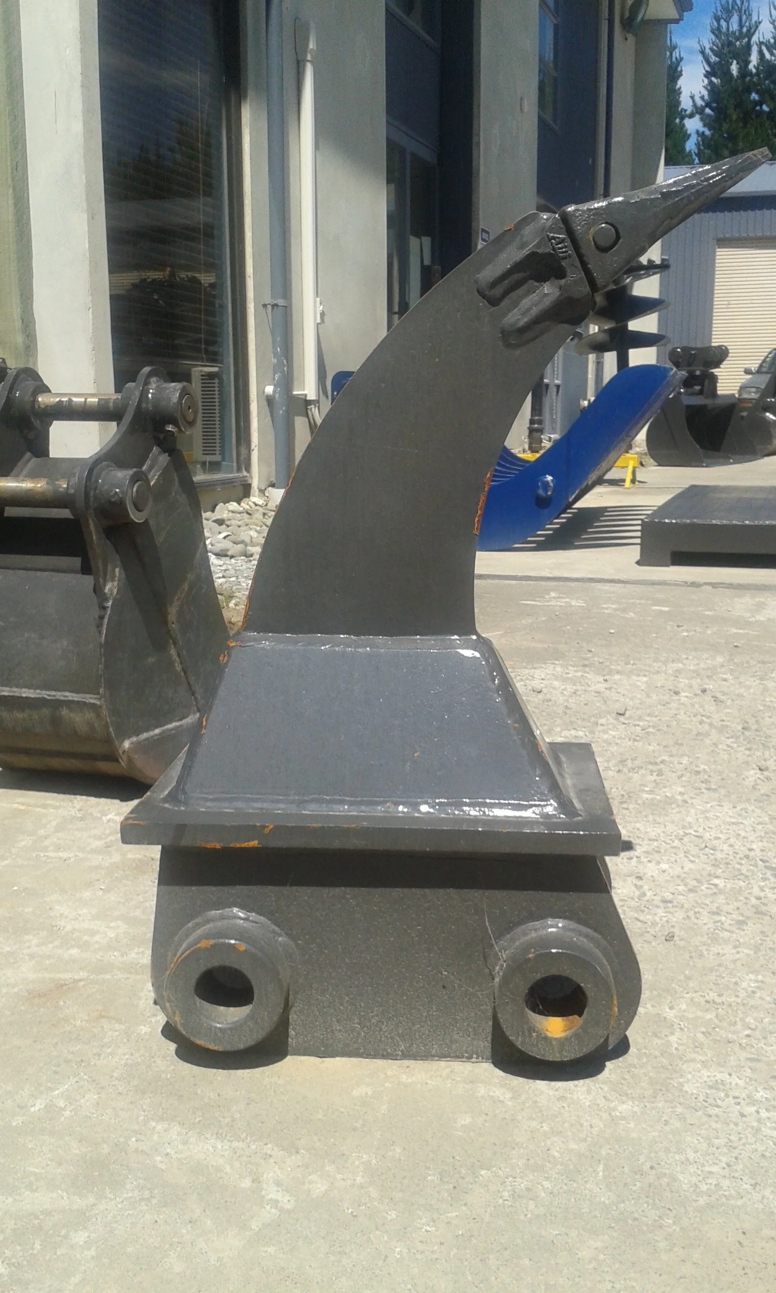 Metal sculpture of a bird head with a pointed beak and detailed eye, mounted on a black base with rounded wheels, outdoors near a building.