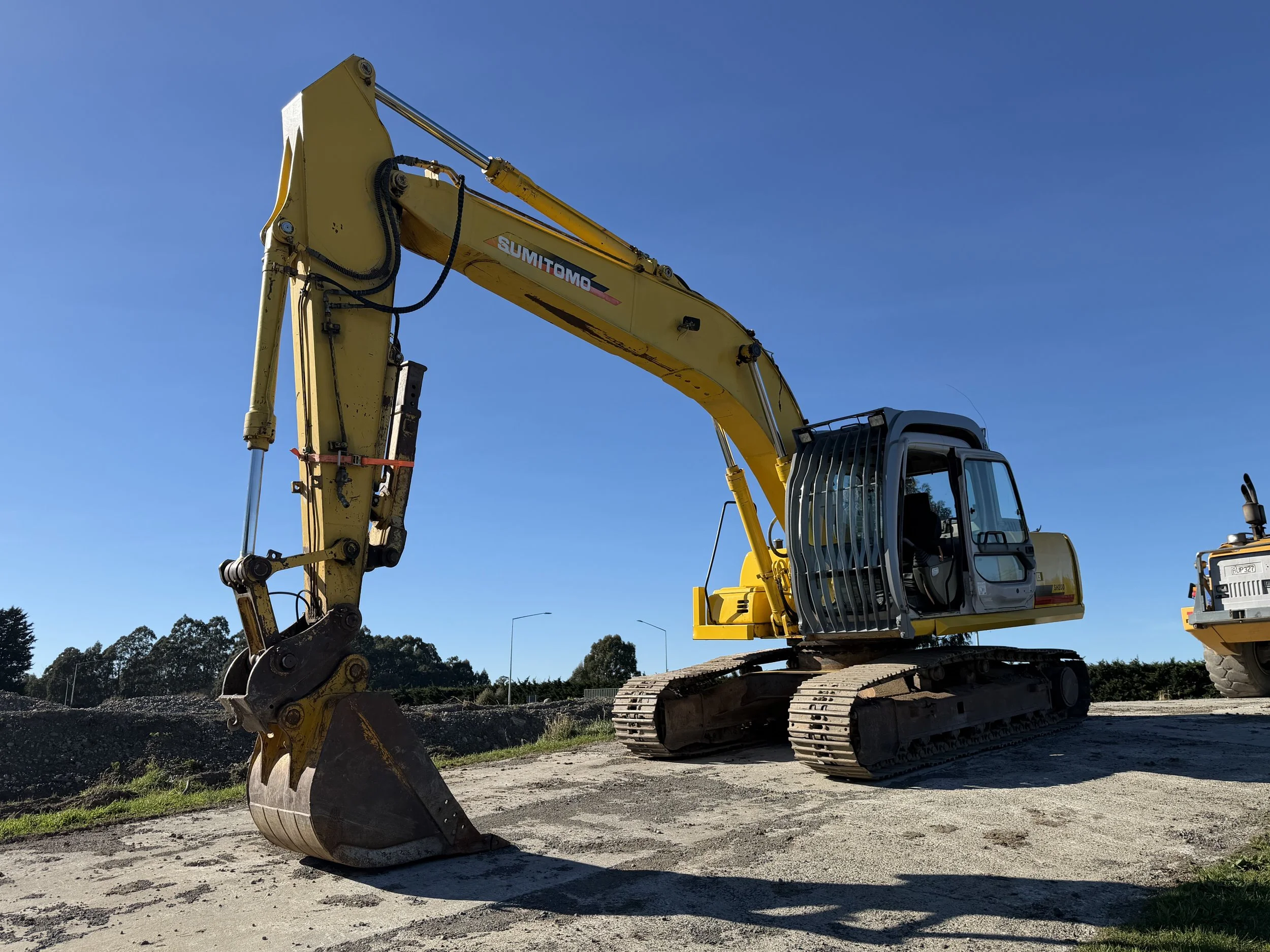 Yellow excavator on a construction site with tracks, digging into dirt under a blue sky.