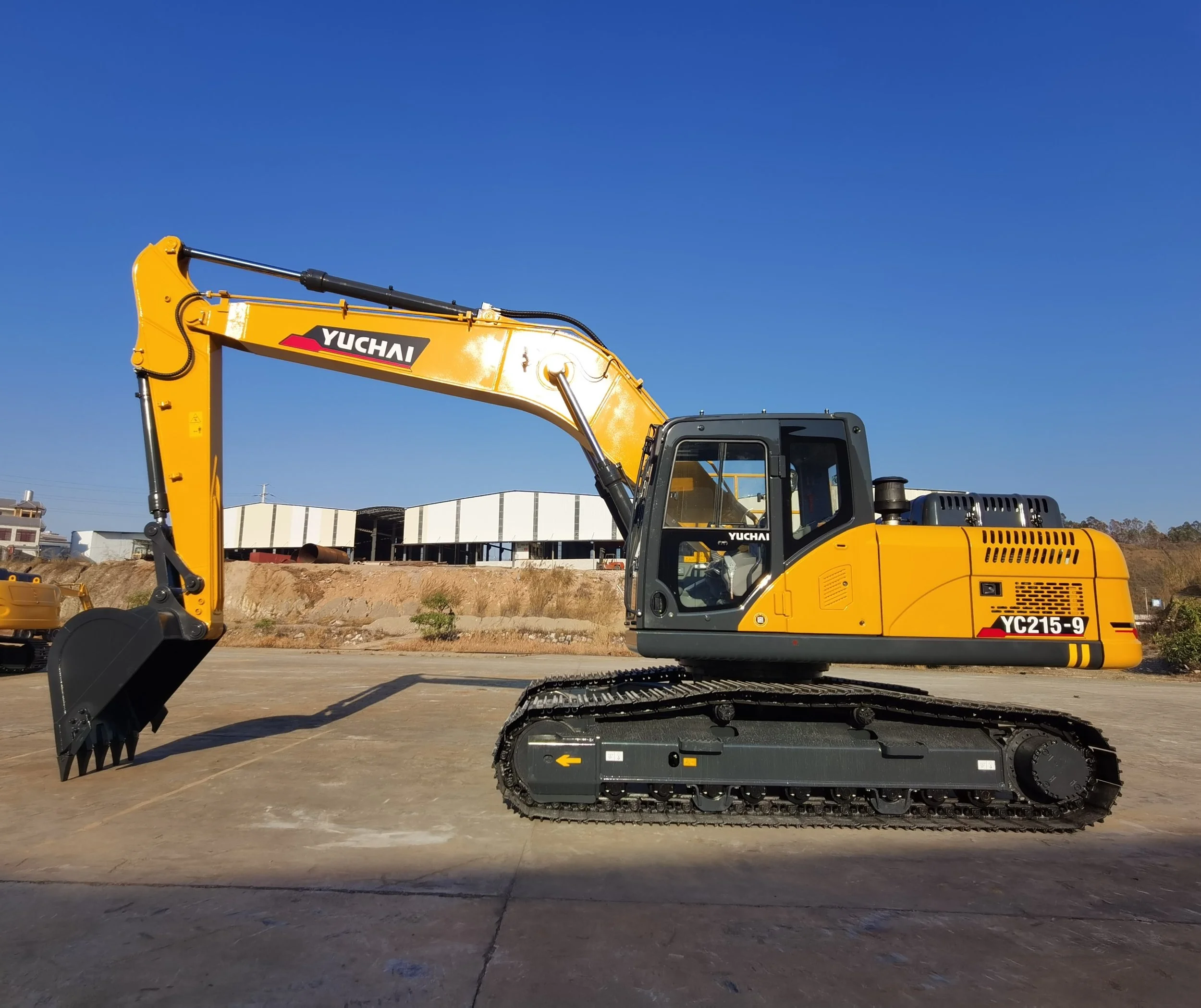Yellow Yuchai excavator with black tracks parked on a construction site under a blue sky.