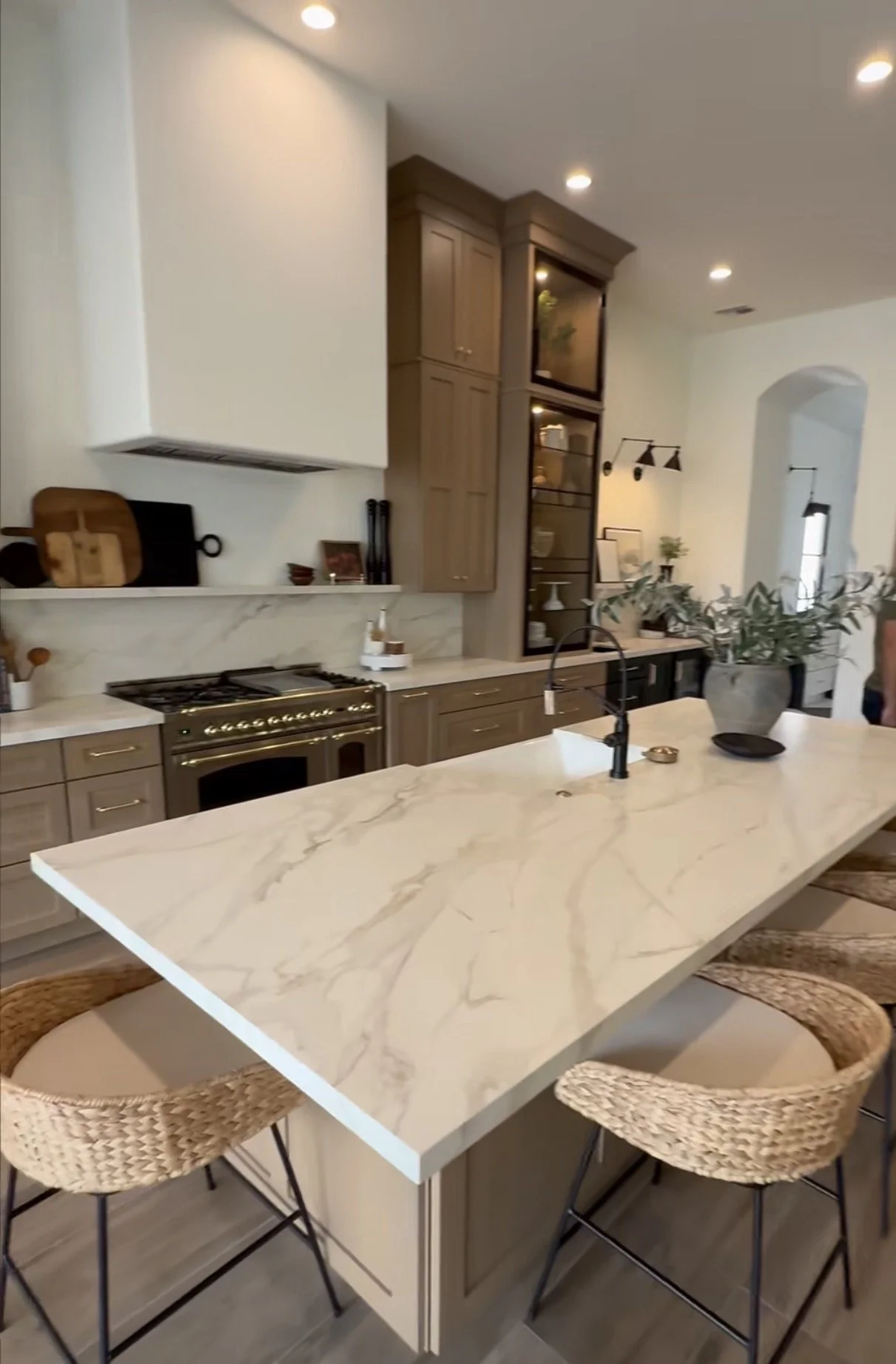 Modern kitchen with a large white marble island, wicker bar stools, wooden cabinets, and built-in appliances.