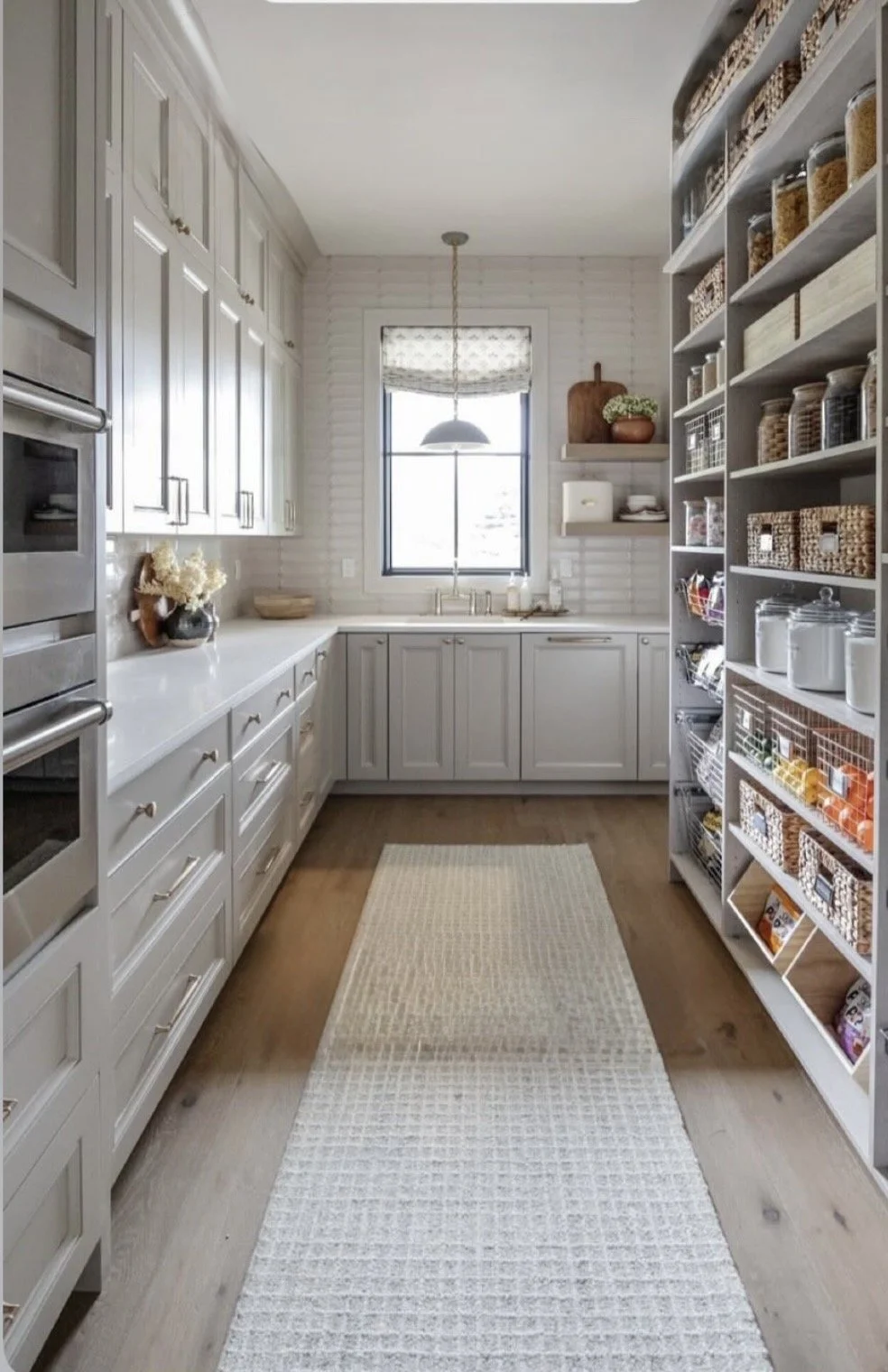 A clean, organized kitchen with white cabinetry, a window above the sink, open shelves, and a storage pantry on the right side.