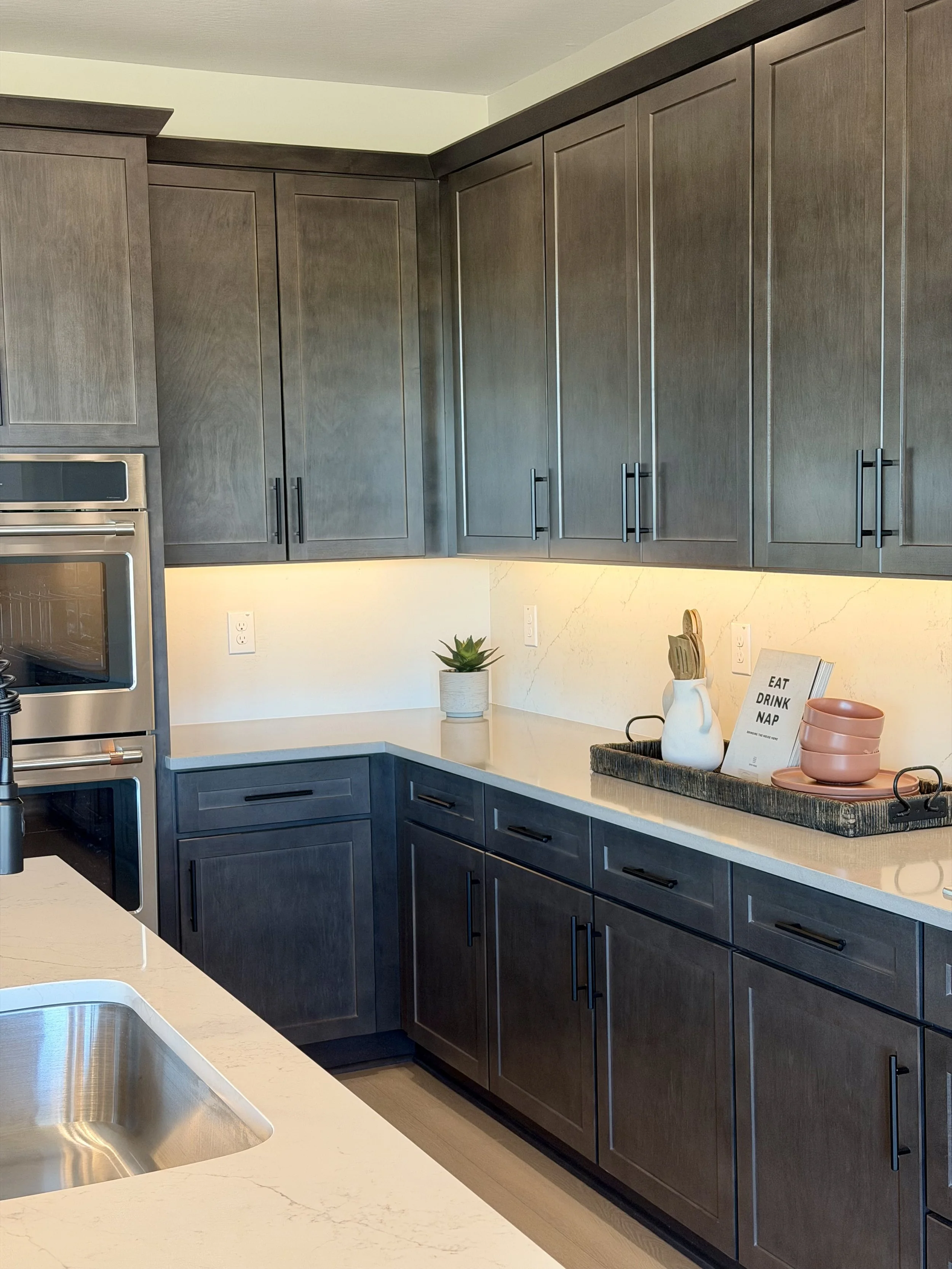 Modern kitchen with dark gray cabinets, white countertops, a small potted plant, and decorative items on the counter.