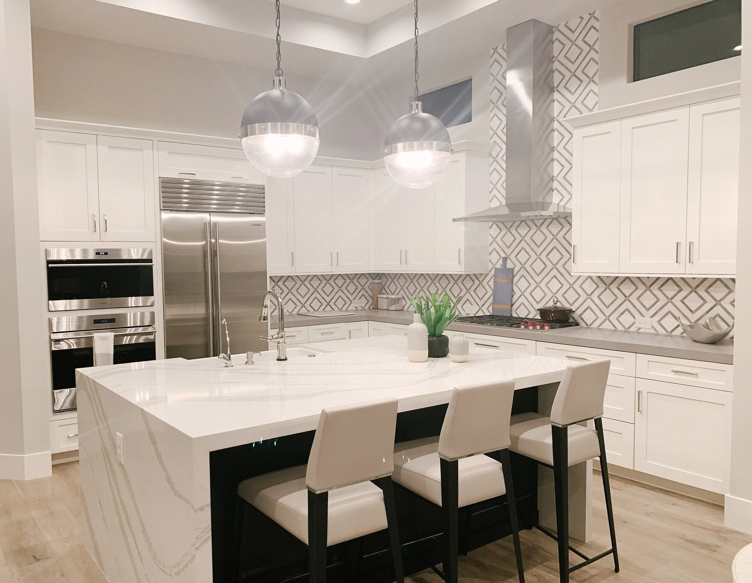 Modern kitchen with white cabinets, stainless steel appliances, a large island with a marble top, and pendant lighting, featuring patterned backsplash tiles.