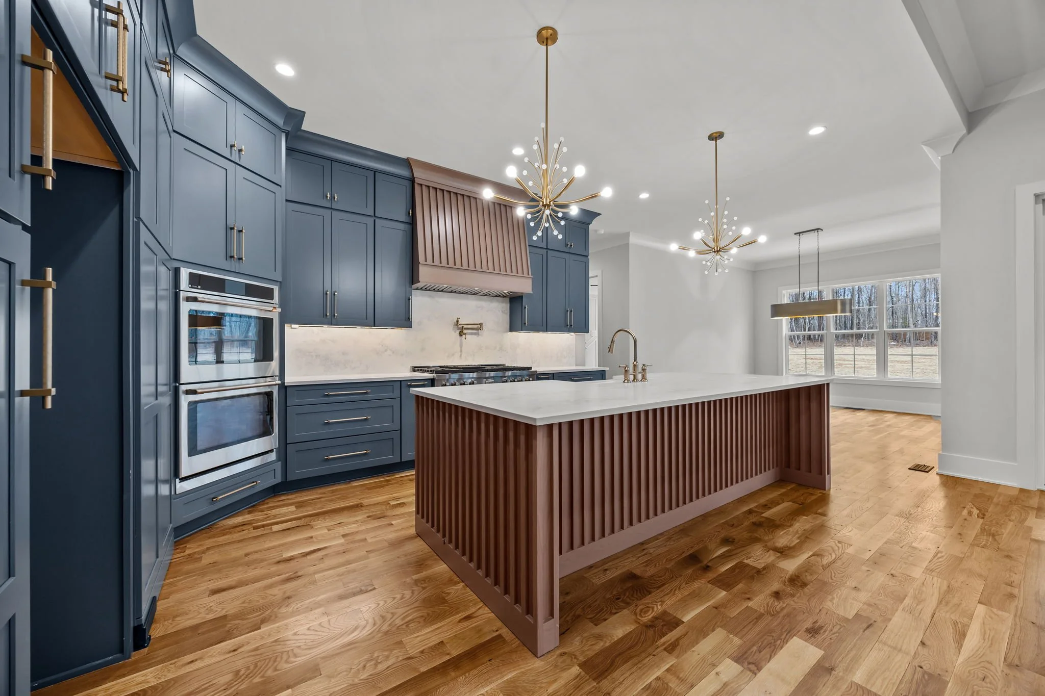 Modern custom kitchen with blue cabinetry, custom range hood, brass lighting fixtures, and fluted wood island with quartz countertop