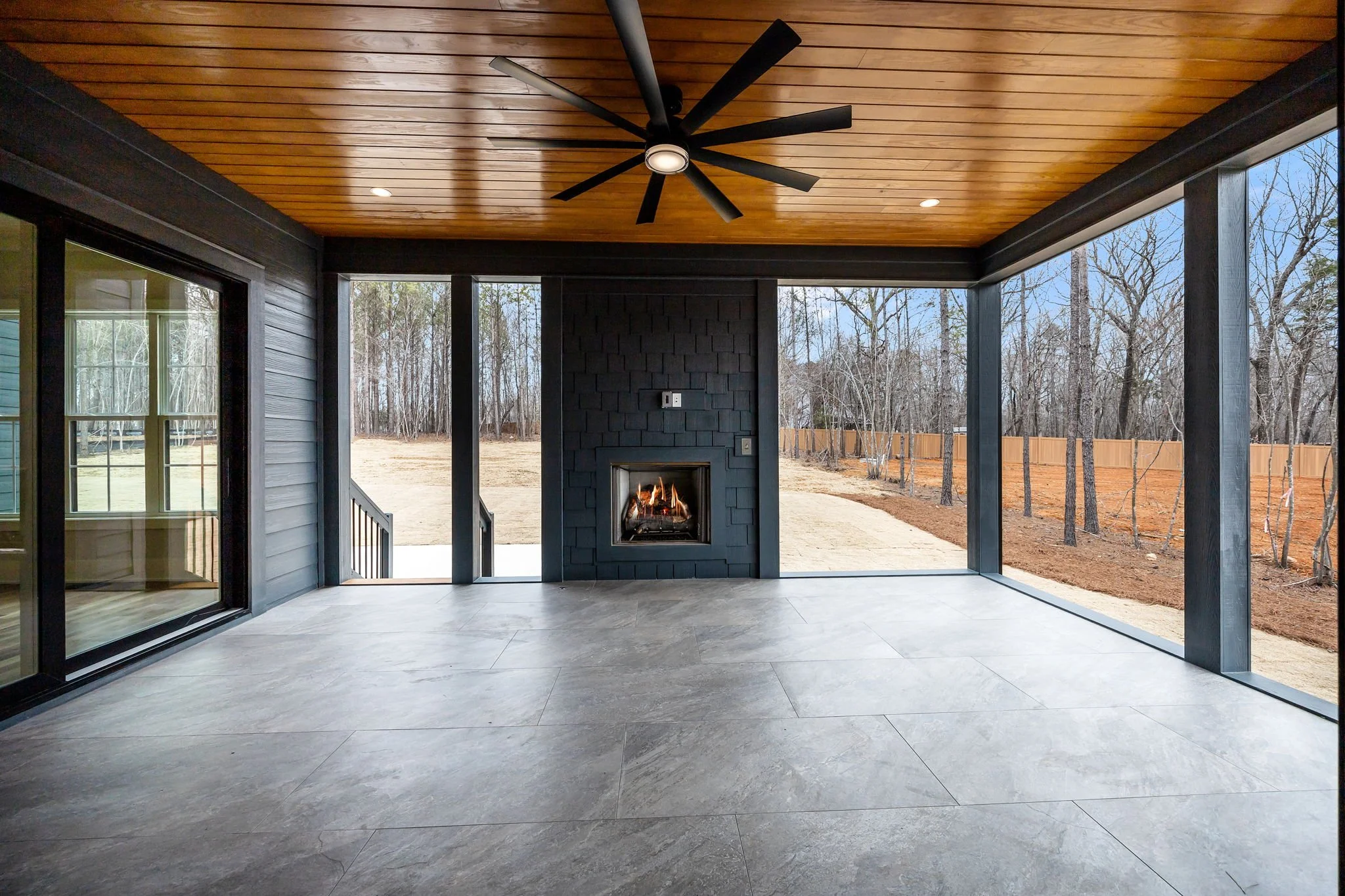 Covered outdoor patio with fireplace, ceiling fan, and seating area attached to rear of custom home