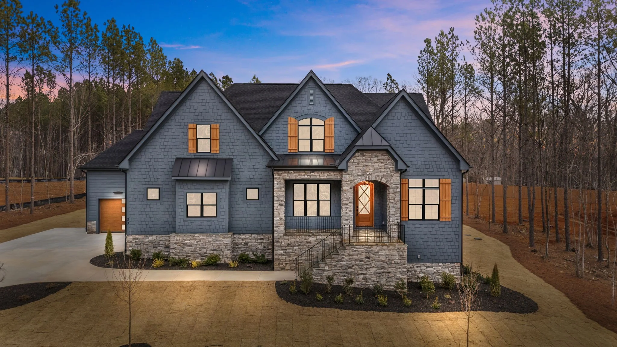 Front view of custom home with blue siding, stone accents, large windows, and covered entry at dusk