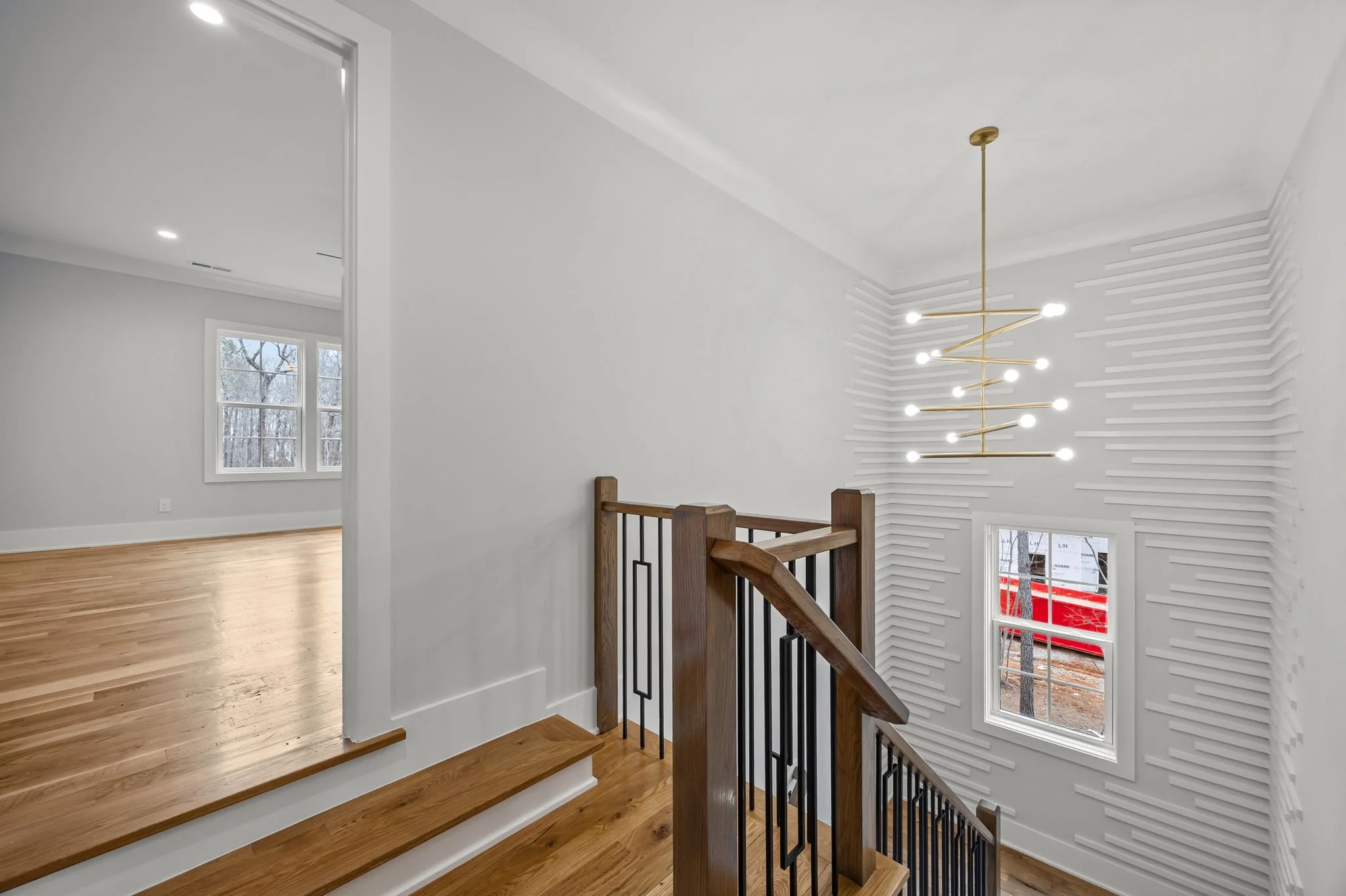Open stairway featuring custom wood railing, black metal balusters, sculptural chandelier, and architectural wall detailing.