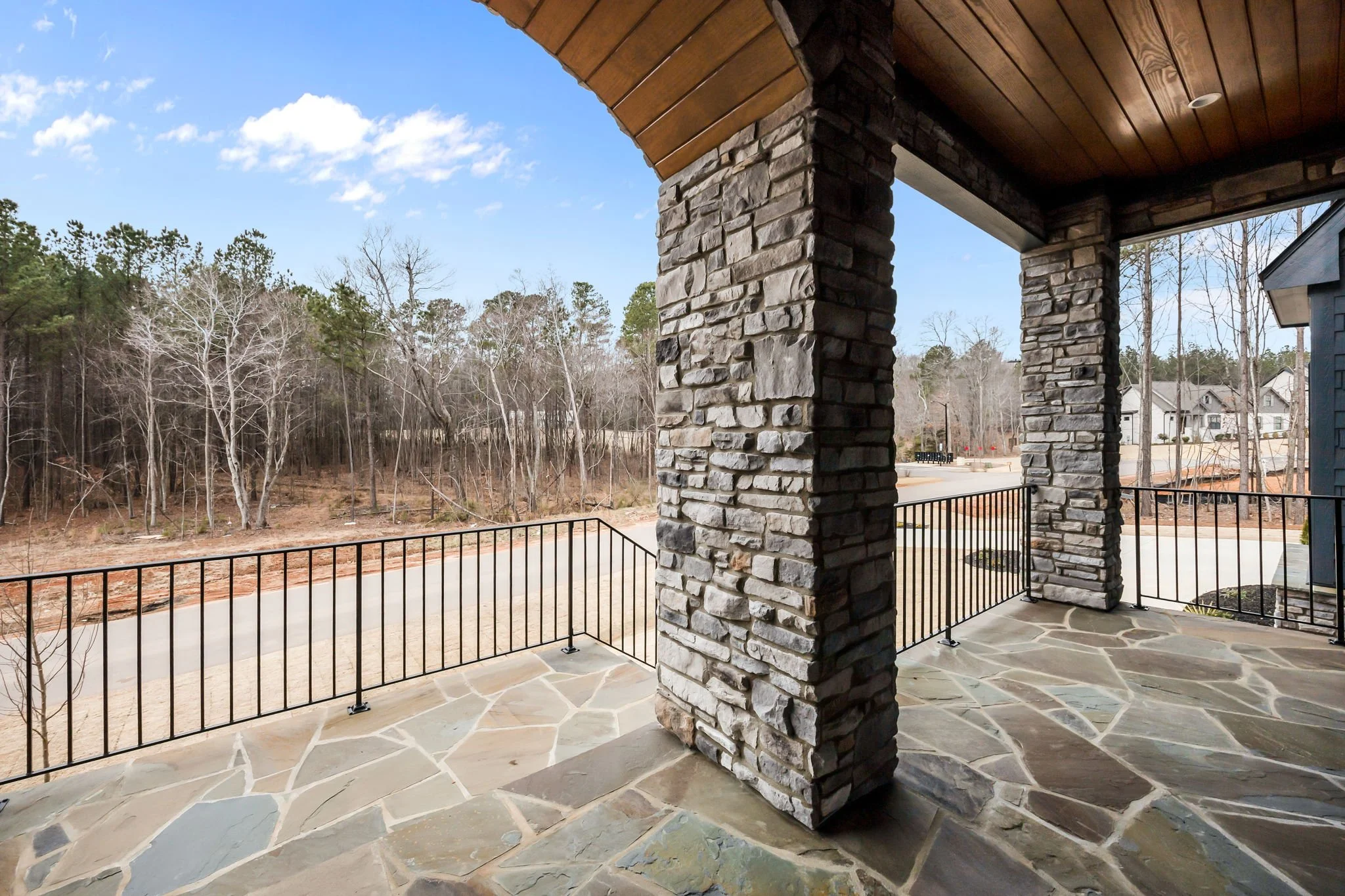Exterior porch detail showing stonework, wood ceiling, and modern black metal railing