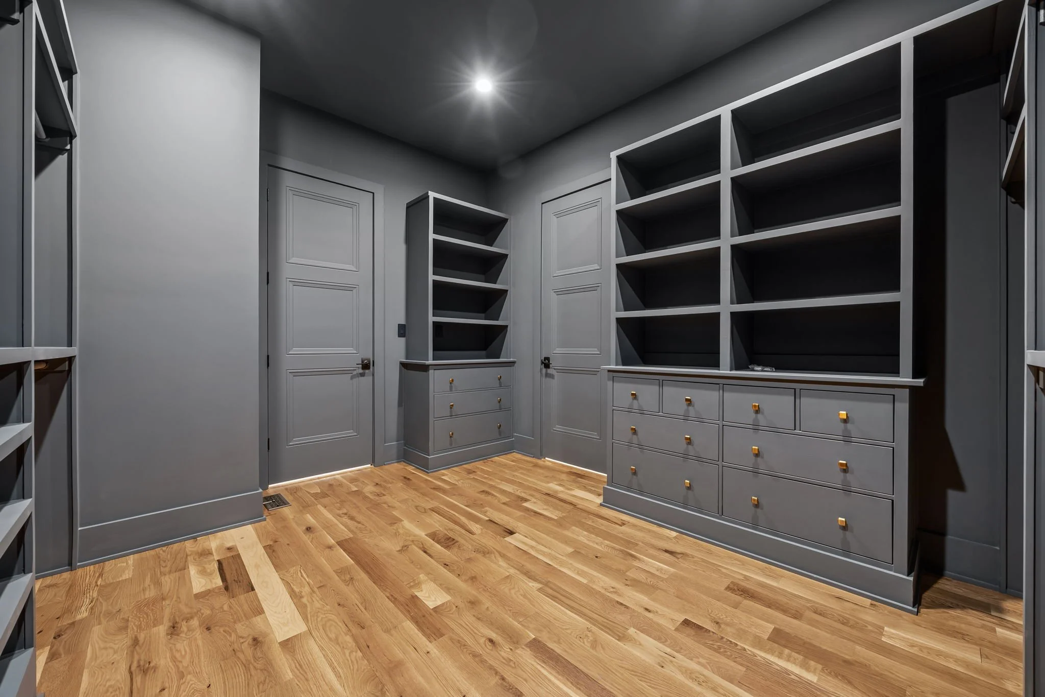 Walk-in closet with built-in shelving, drawers, and hanging space, featuring gray cabinetry, brass hardware, and hardwood flooring.