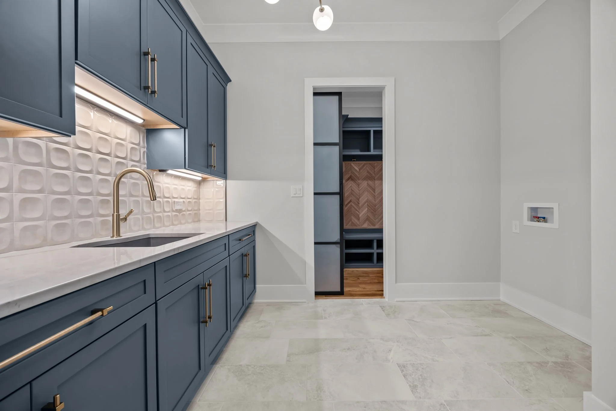 Laundry and mudroom with blue cabinets, quartz countertops, utility sink, tile flooring, and built-in storage
