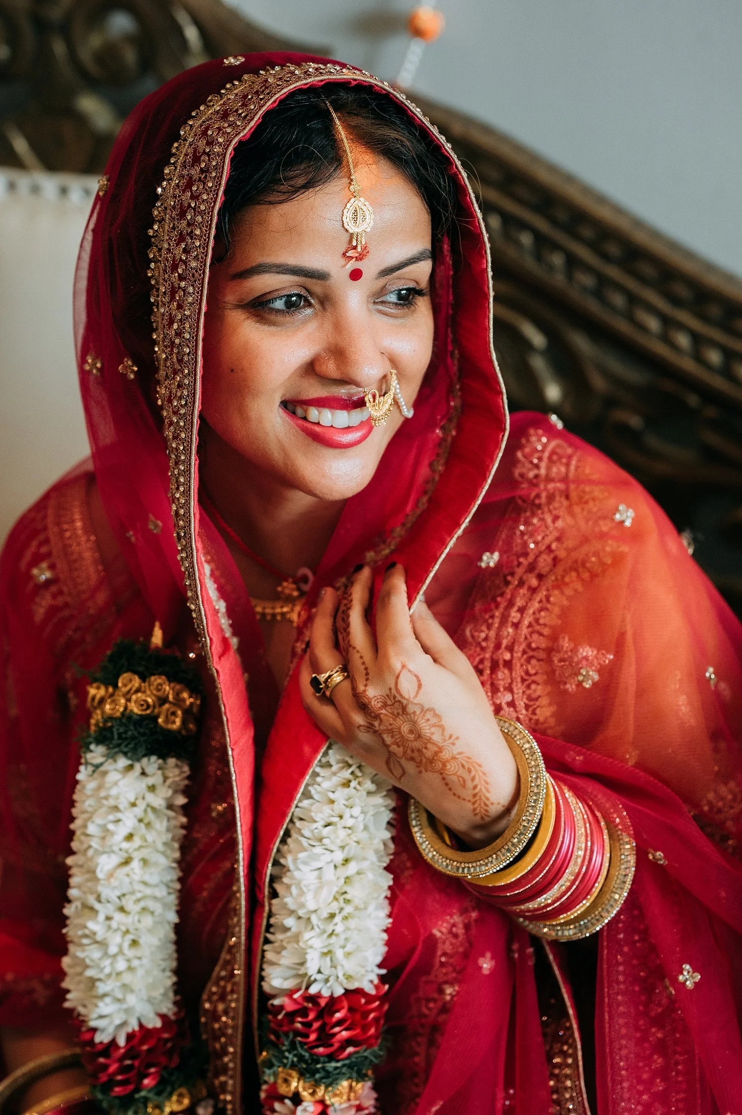  Joyful portrait of the Indian bride smiling, highlighting her traditional bridal jewelry and red lip. 